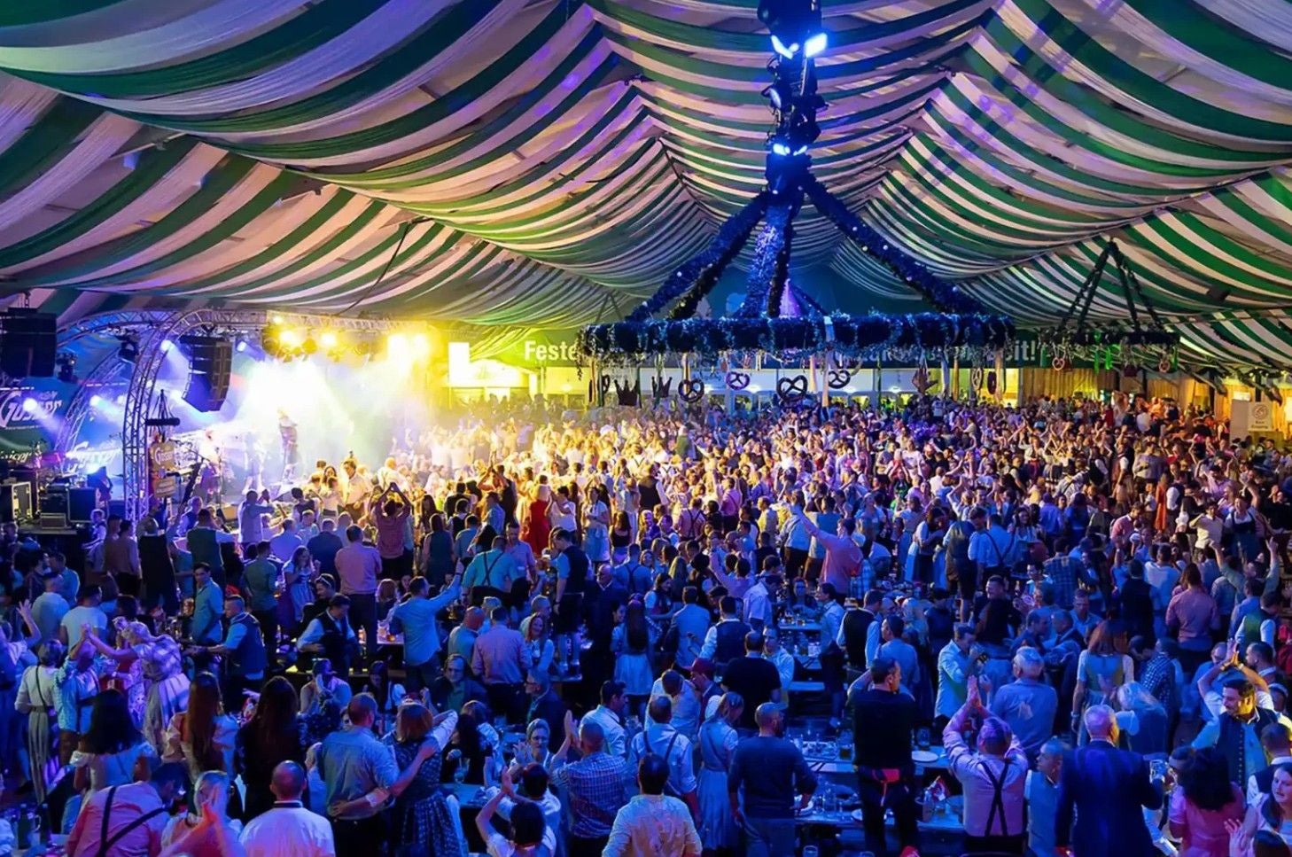 Großes Festzelt mit vielen Menschen bei der Wiener Kaiser Wiesn, bunte Beleuchtung und Musikbühne.