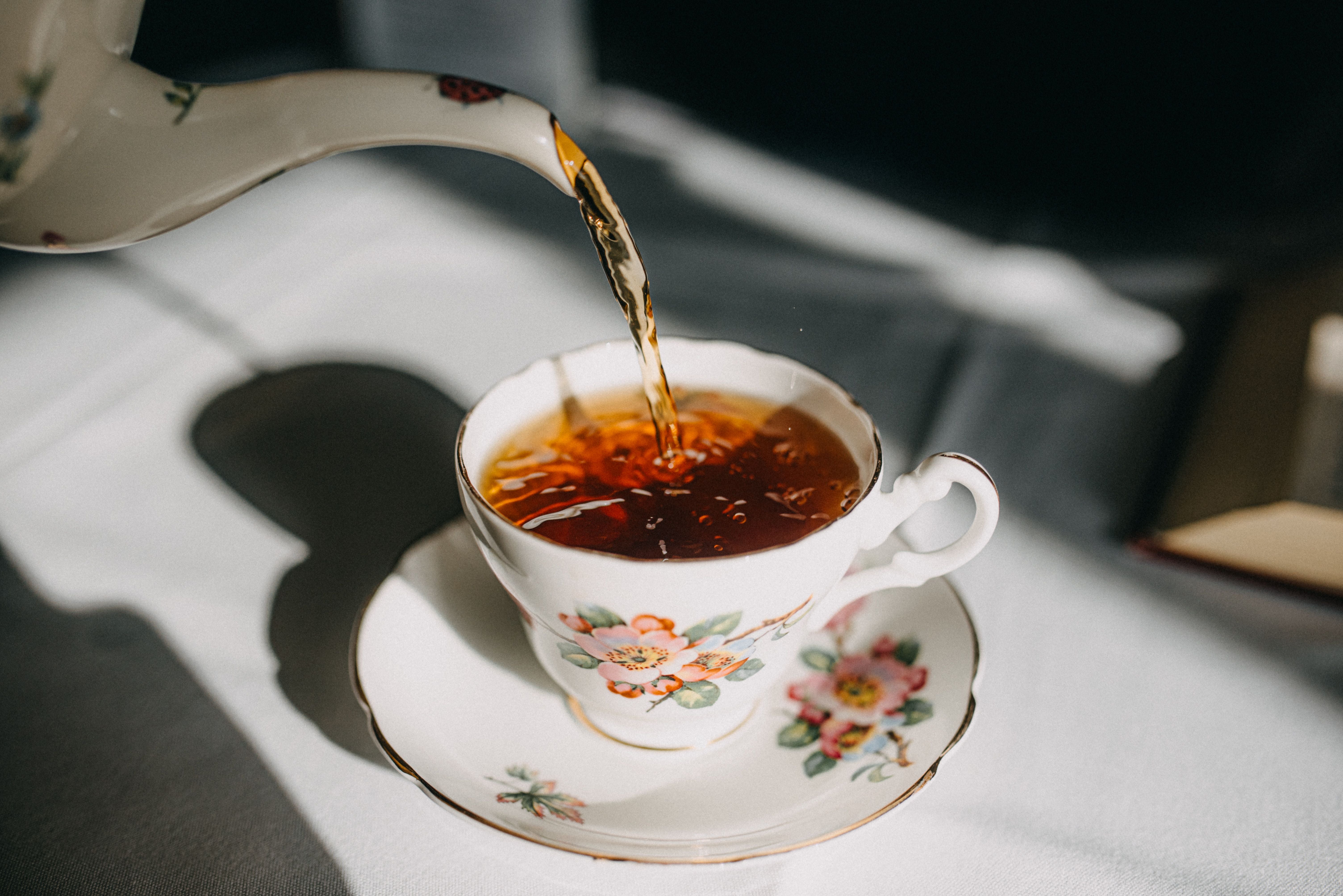 Tee wird in eine geblümte Teetasse auf einer passenden Untertasse gegossen.