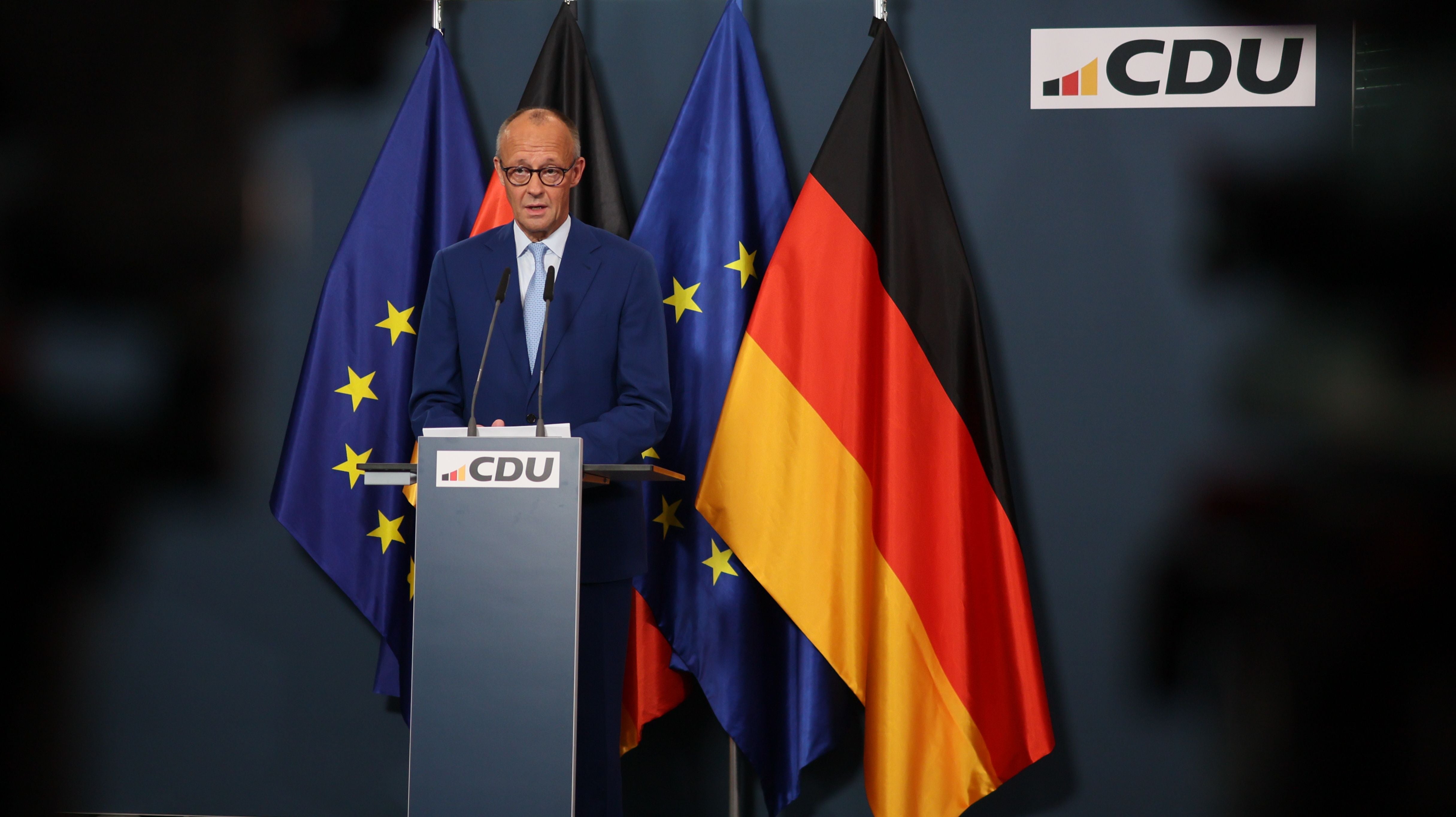 Ein Mann spricht am CDU-Pult vor deutschen und EU-Flaggen bei einer Pressekonferenz.