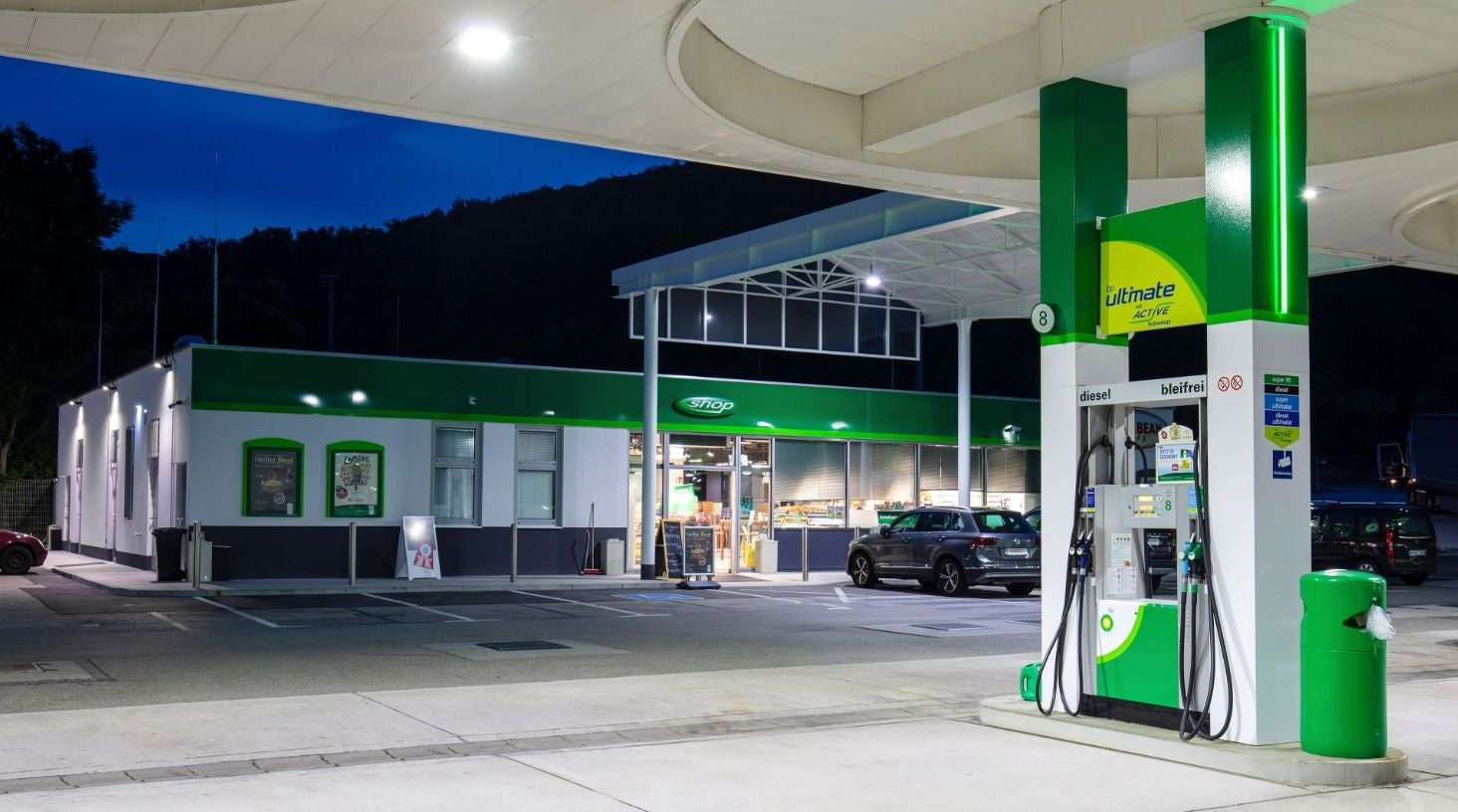 Beleuchtete BP-Tankstelle mit Zapfsäule und Shop bei Nacht. Ein Auto steht vor dem Gebäude.