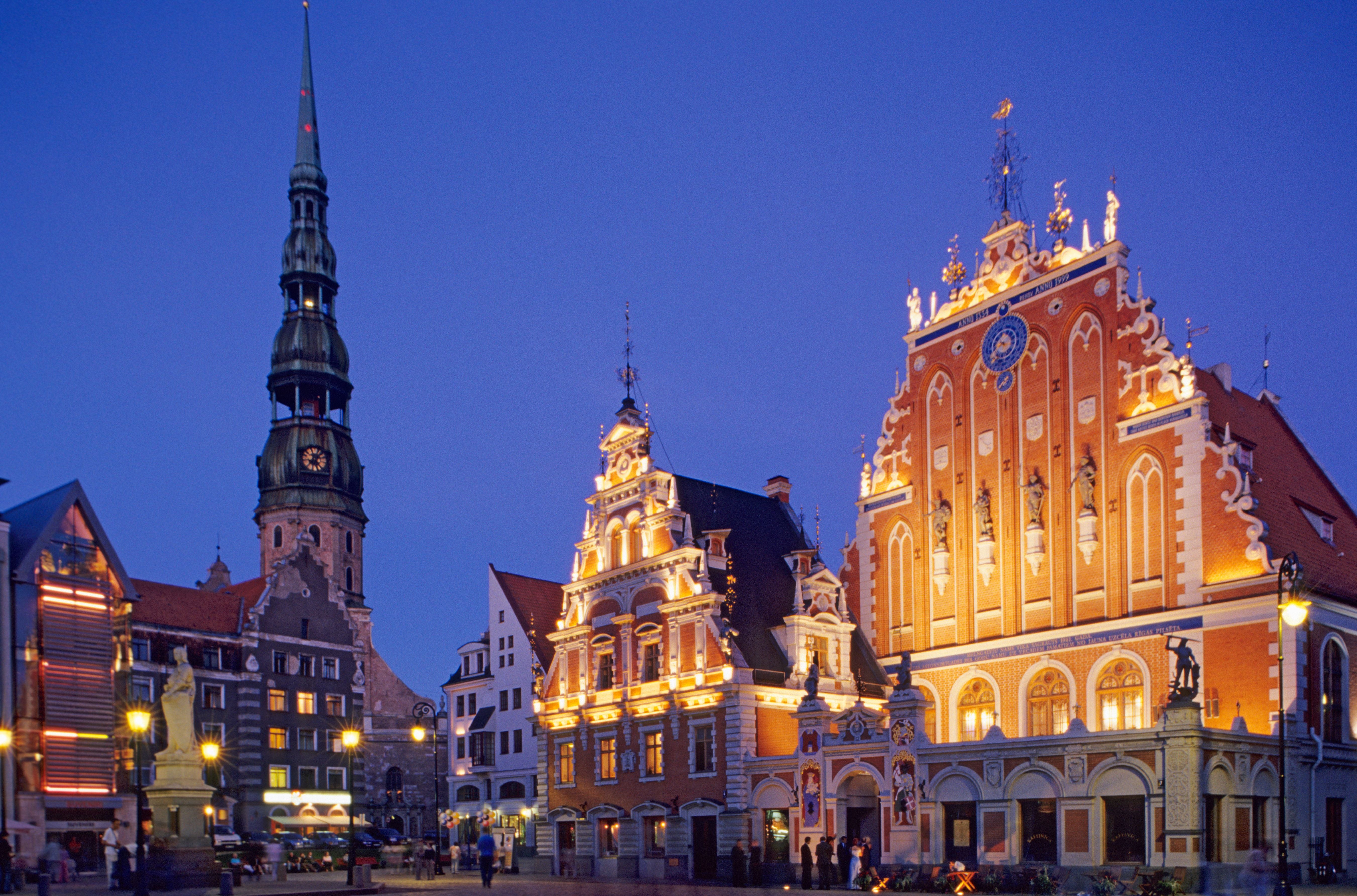 Abendliche Ansicht des Schwarzhaupter Hauses und der St. Petrikirche in Riga mit beleuchteten Fassaden.