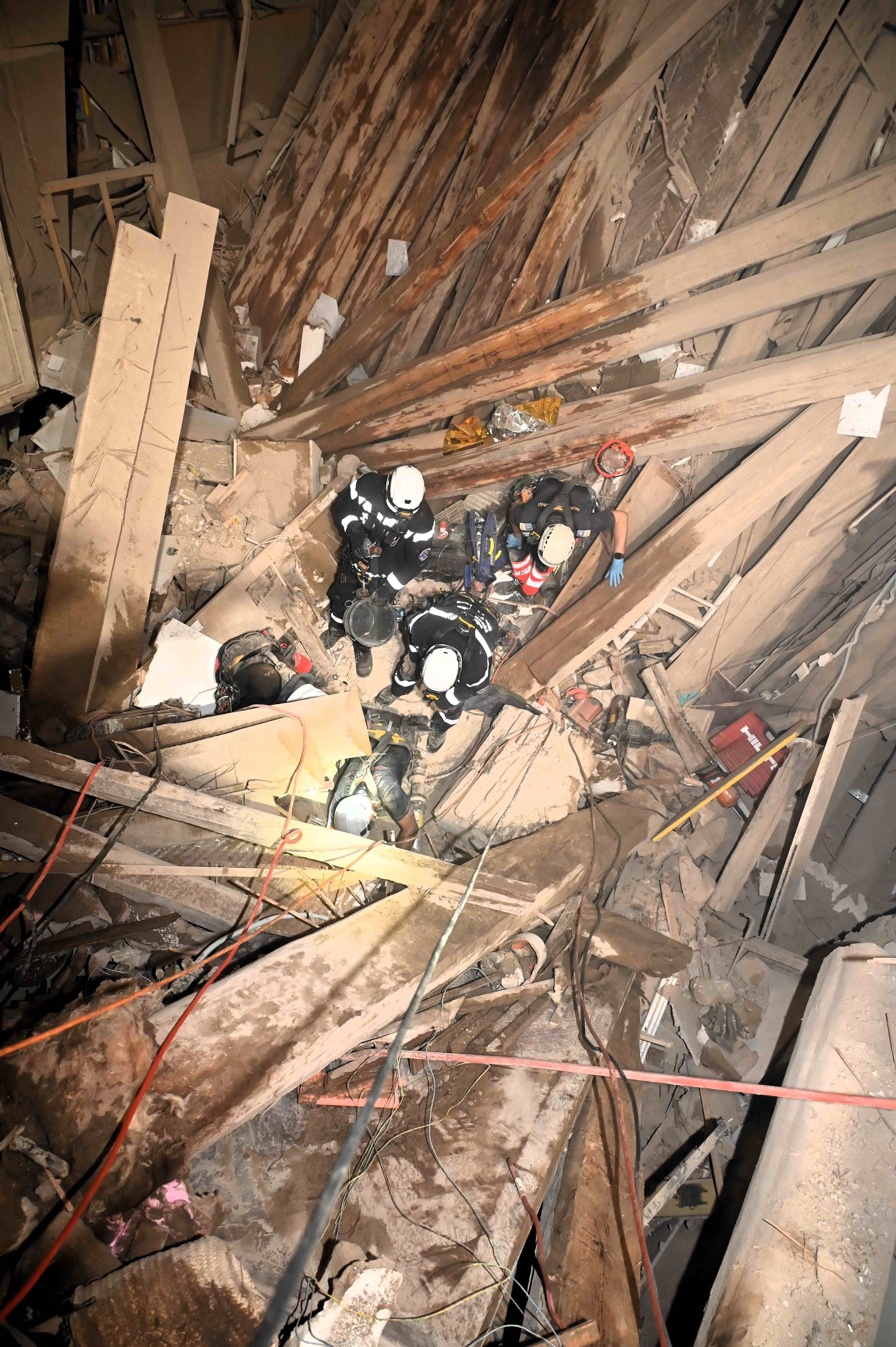 Mehrere Einsatzkräfte arbeiten inmitten eingestürzter Holzbalken und Trümmern in einem Gebäude.