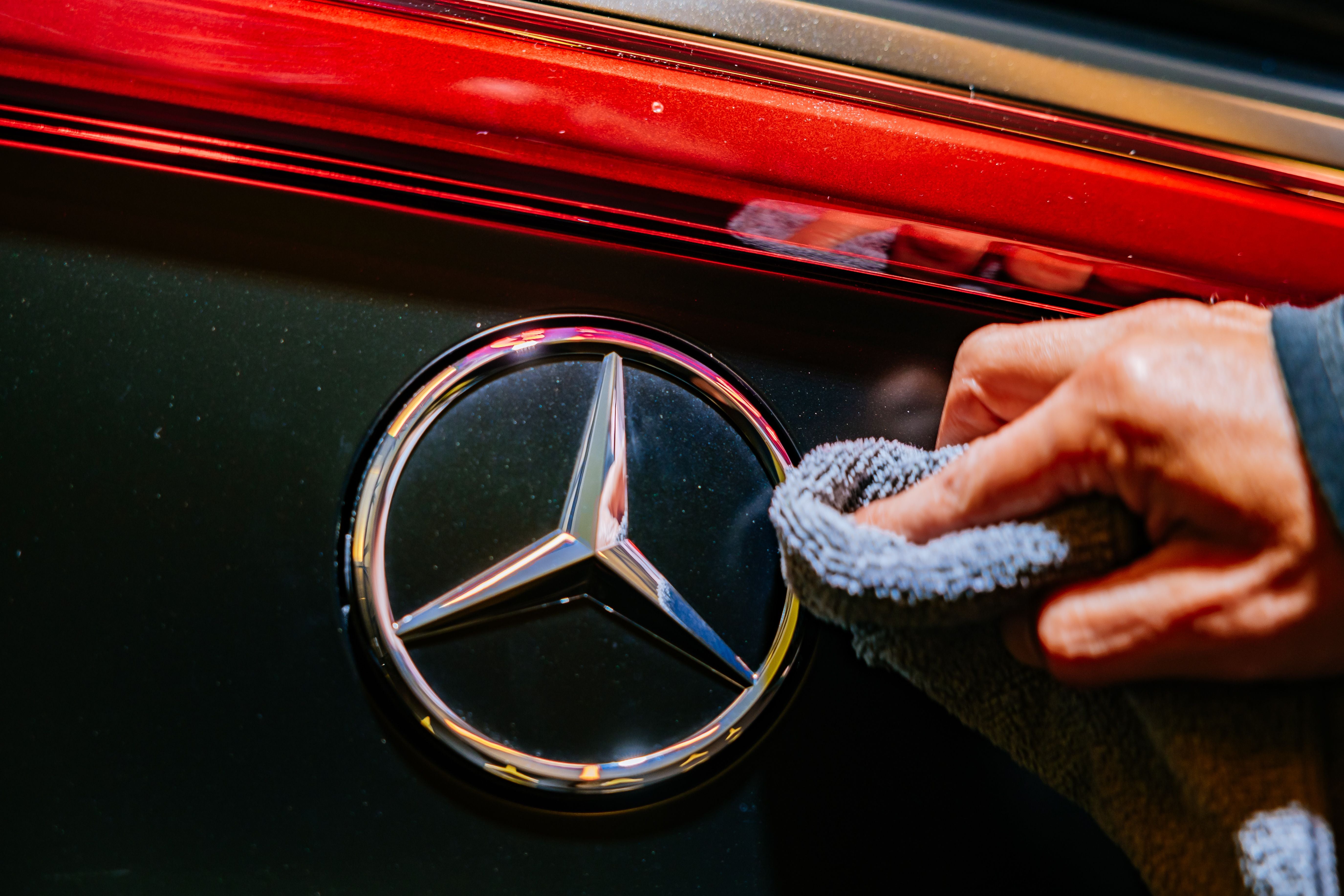 Hand poliert das Mercedes-Benz-Logo an einem schwarzen Auto mit roter Zierleiste.