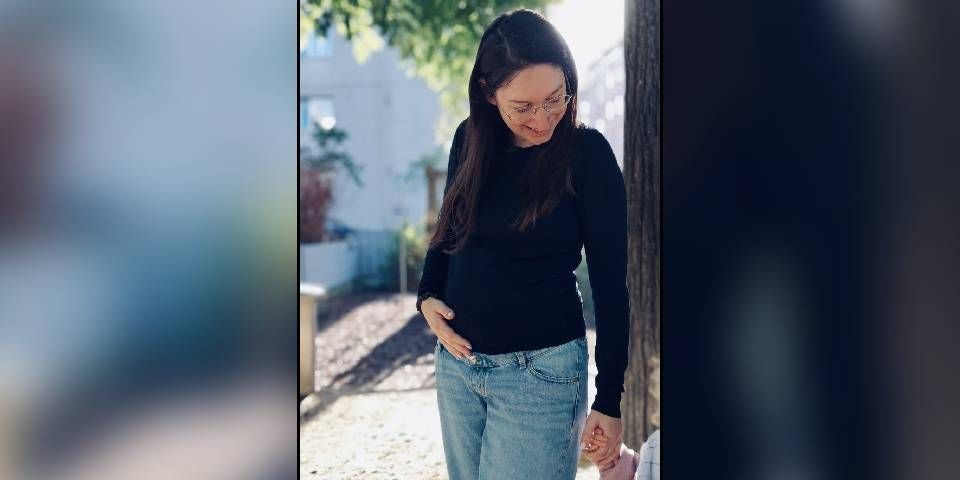 Frau mit Brille und langen Haaren steht draußen und schaut lächelnd nach unten.