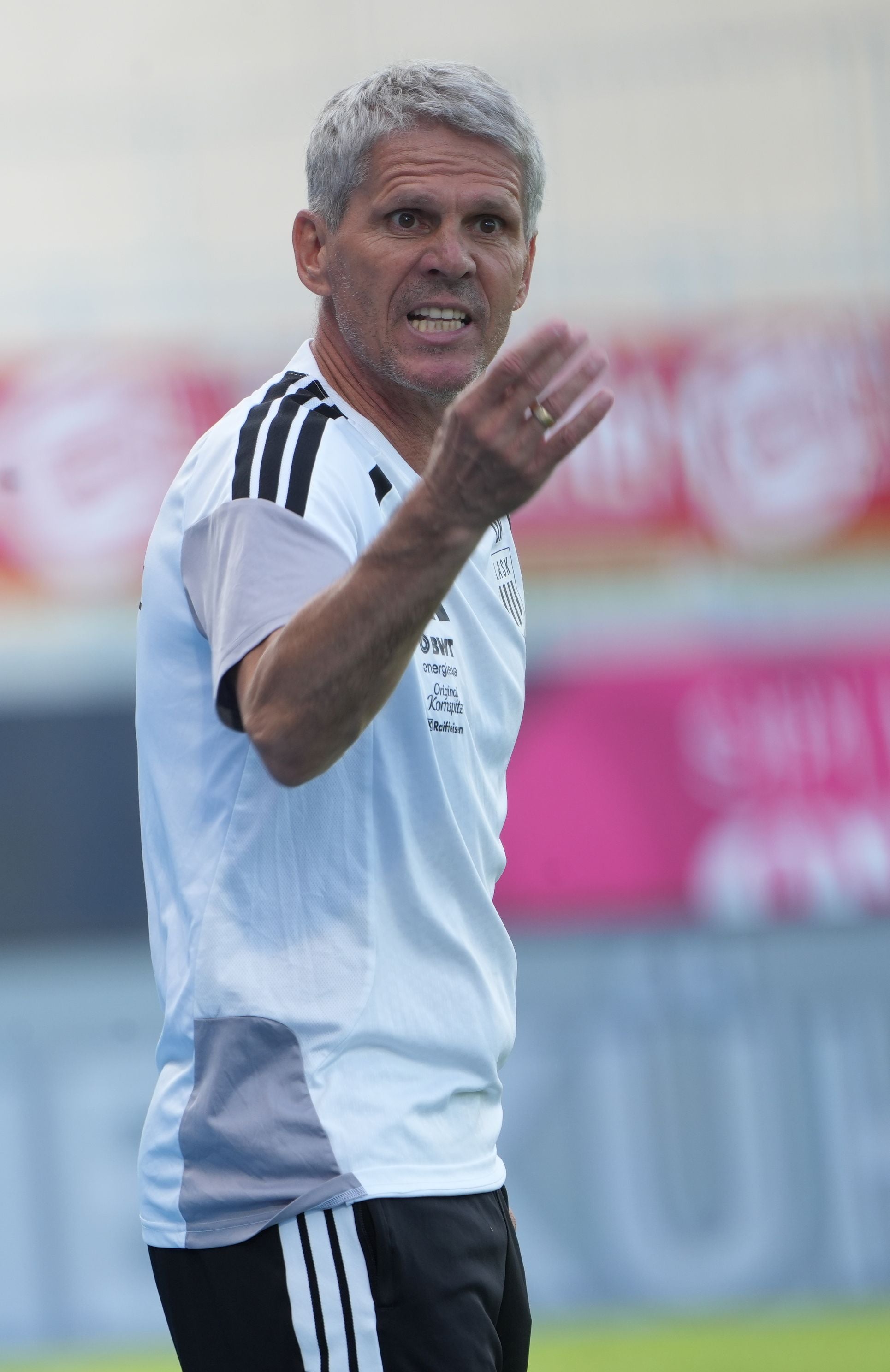 Trainer in weißem Trikot gestikuliert energisch am Spielfeldrand während eines Fußballspiels.
