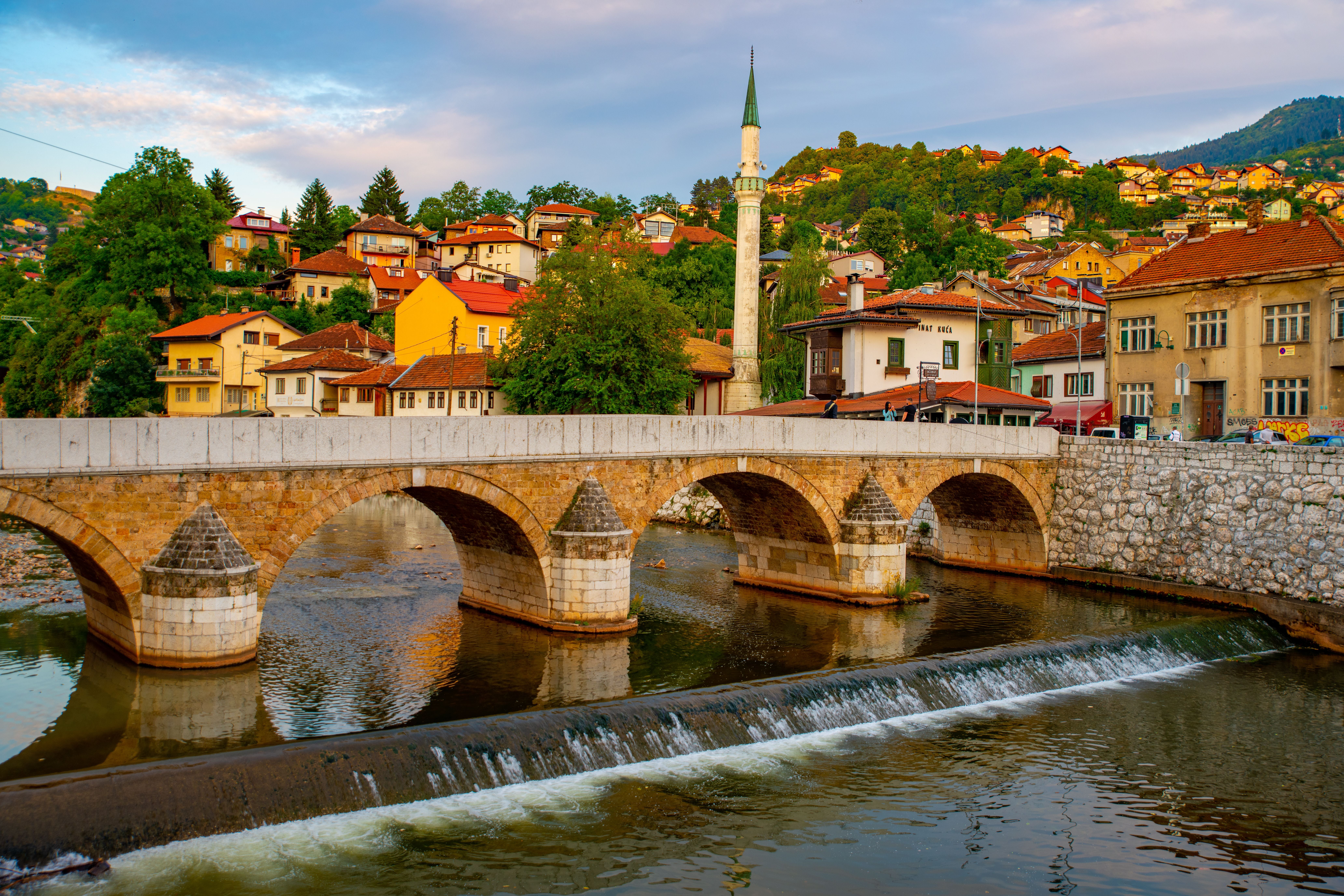 Die Lateinische Brücke in Sarajevo überspannt den Fluss Miljacka, im Hintergrund bunte Häuser.