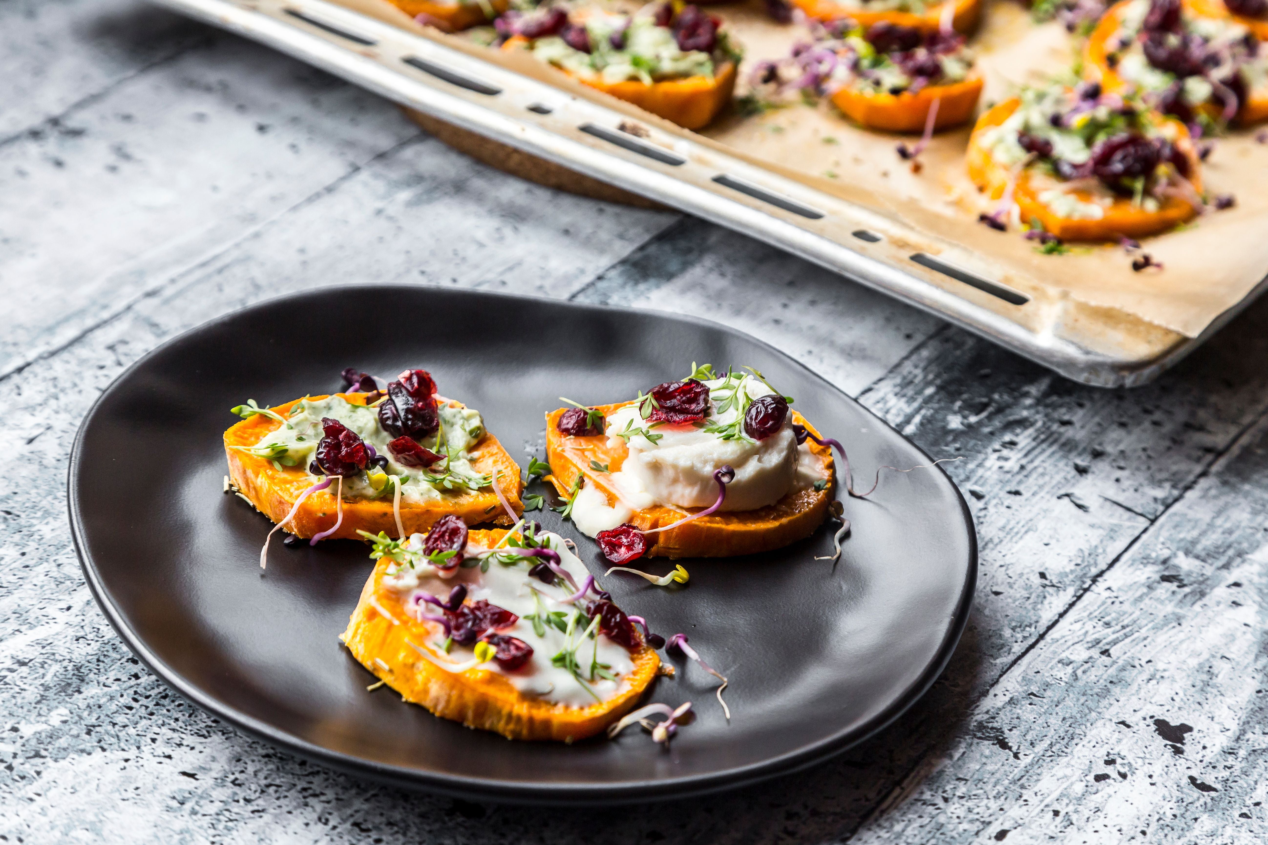 Drei Kürbis Bites mit Käse, Kräutern und Cranberries auf schwarzem Teller.