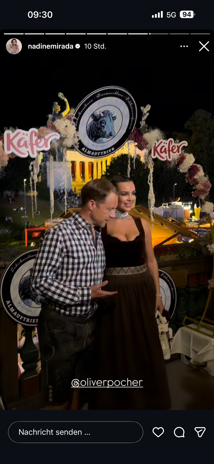 Ein Mann und eine Frau posieren in Tracht vor festlicher Oktoberfest-Dekoration bei Nacht.