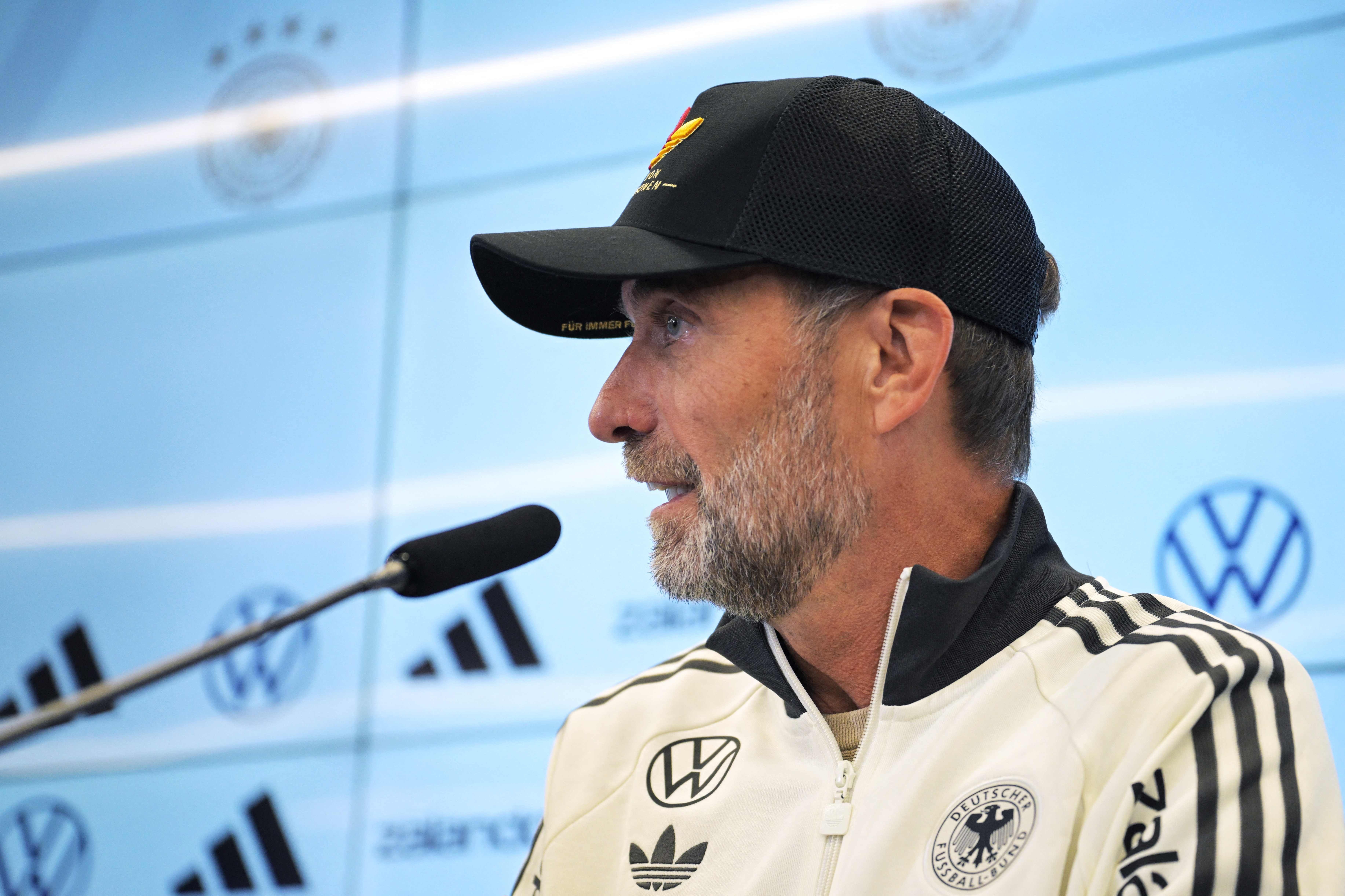 Ein Mann im DFB-Trainingsanzug und Basecap spricht bei einer Pressekonferenz ins Mikrofon.