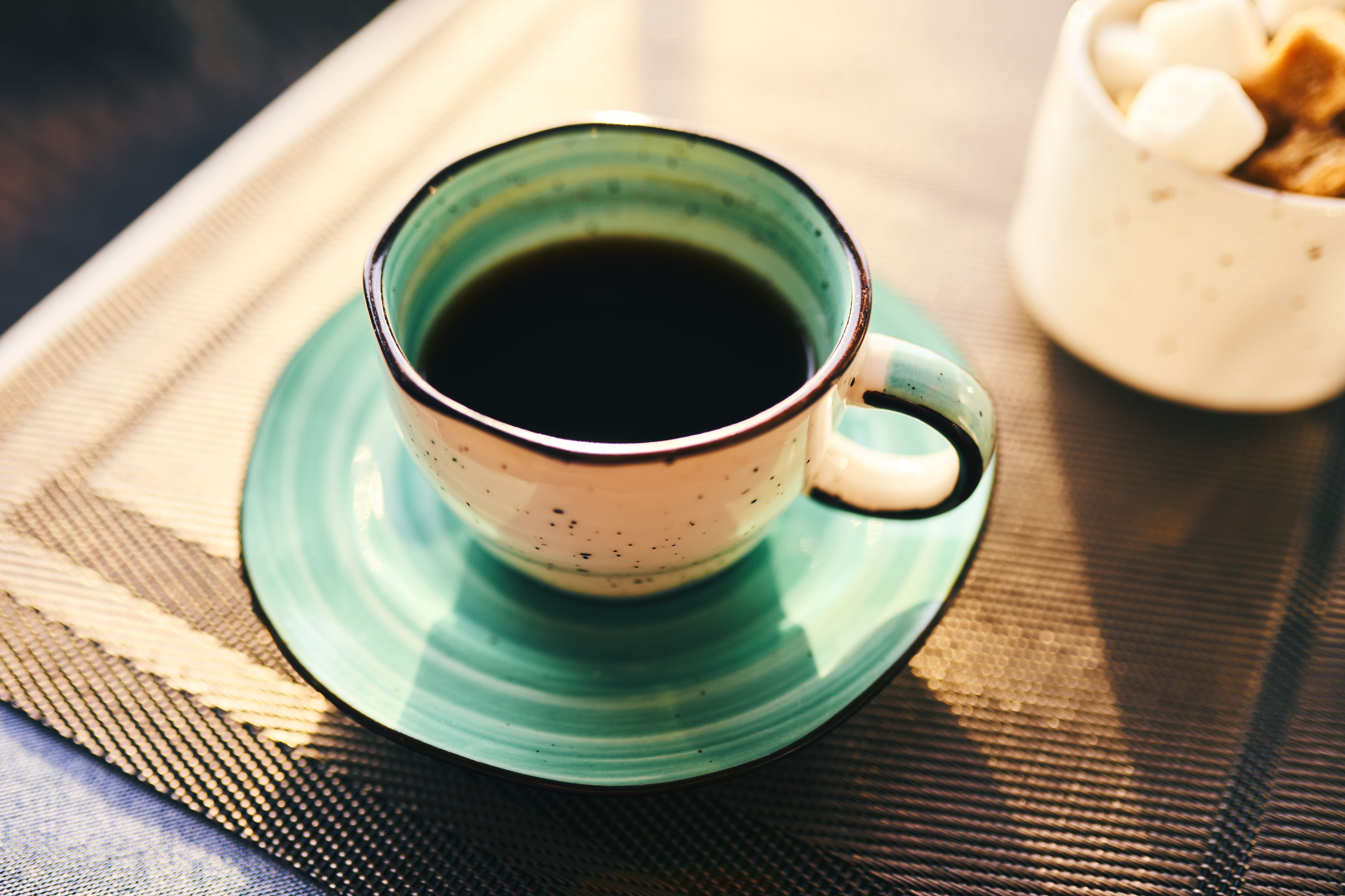 Eine türkisfarbene Kaffeetasse mit schwarzem Kaffee steht auf einer passenden Untertasse.