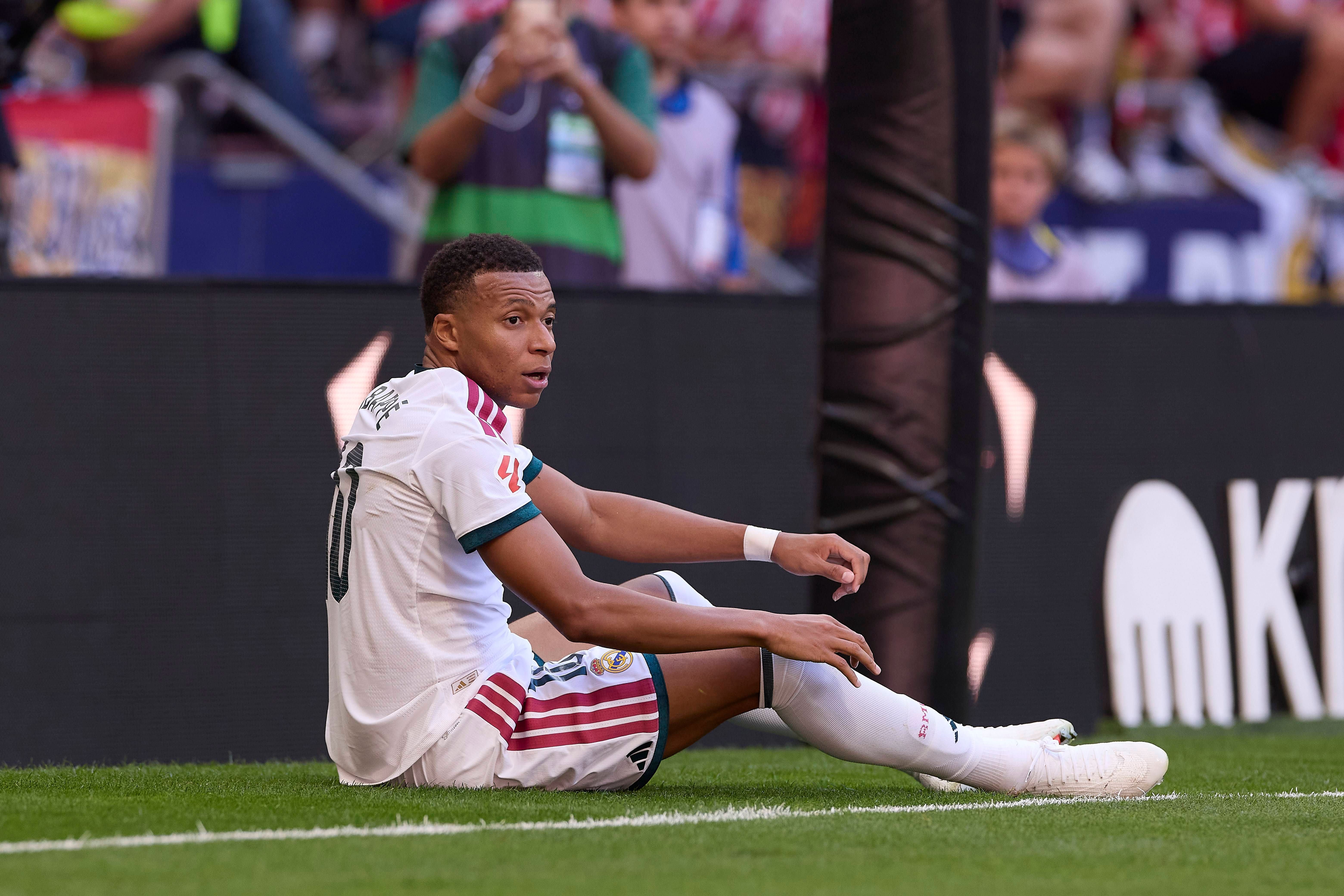 Kylian Mbappé sitzt im Real-Madrid-Trikot am Spielfeldrand während eines Fußballspiels.