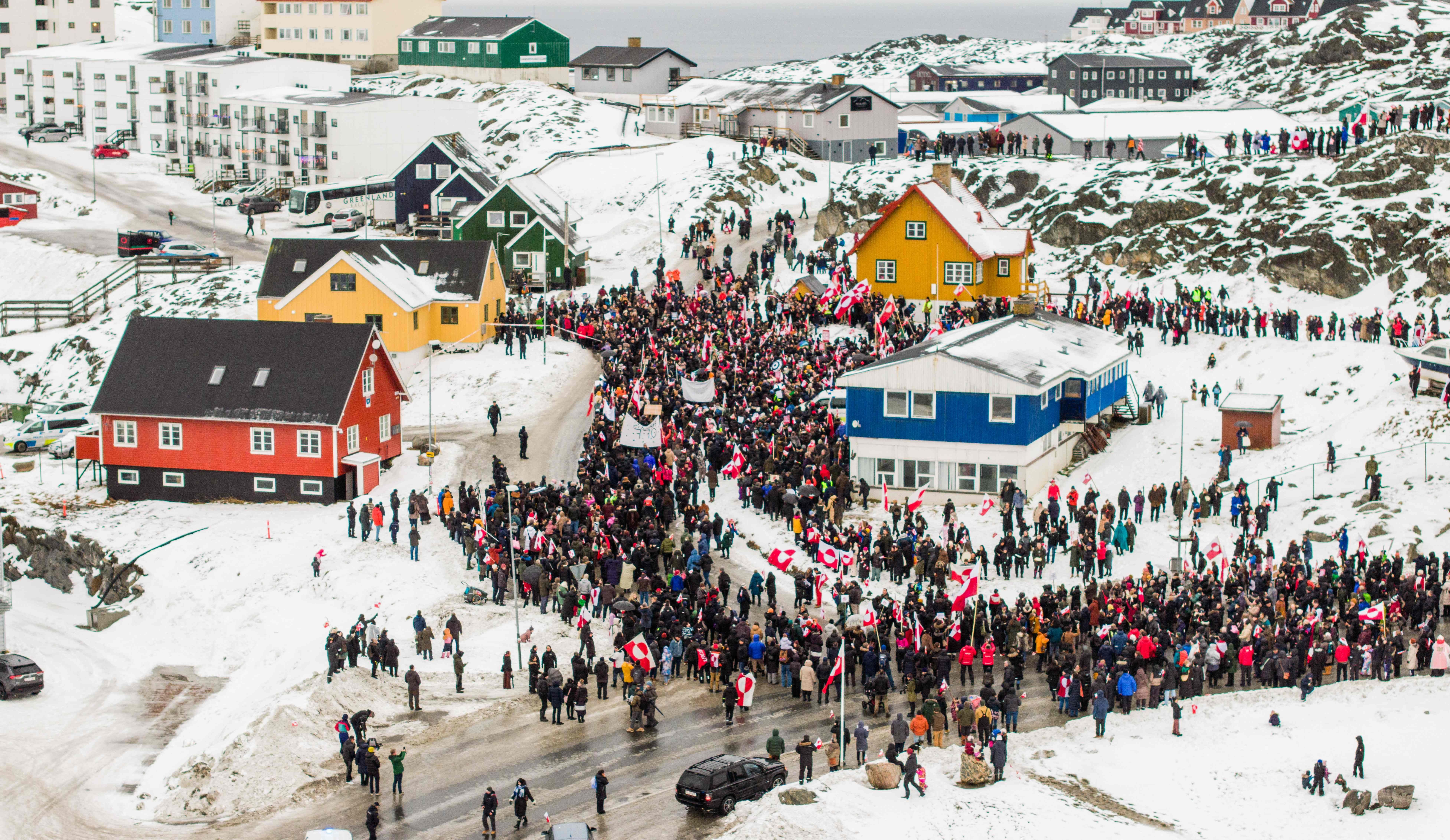 Menschenmenge protestiert mit Fahnen und Transparenten auf verschneiter Straße in Nuuk, Grönland.