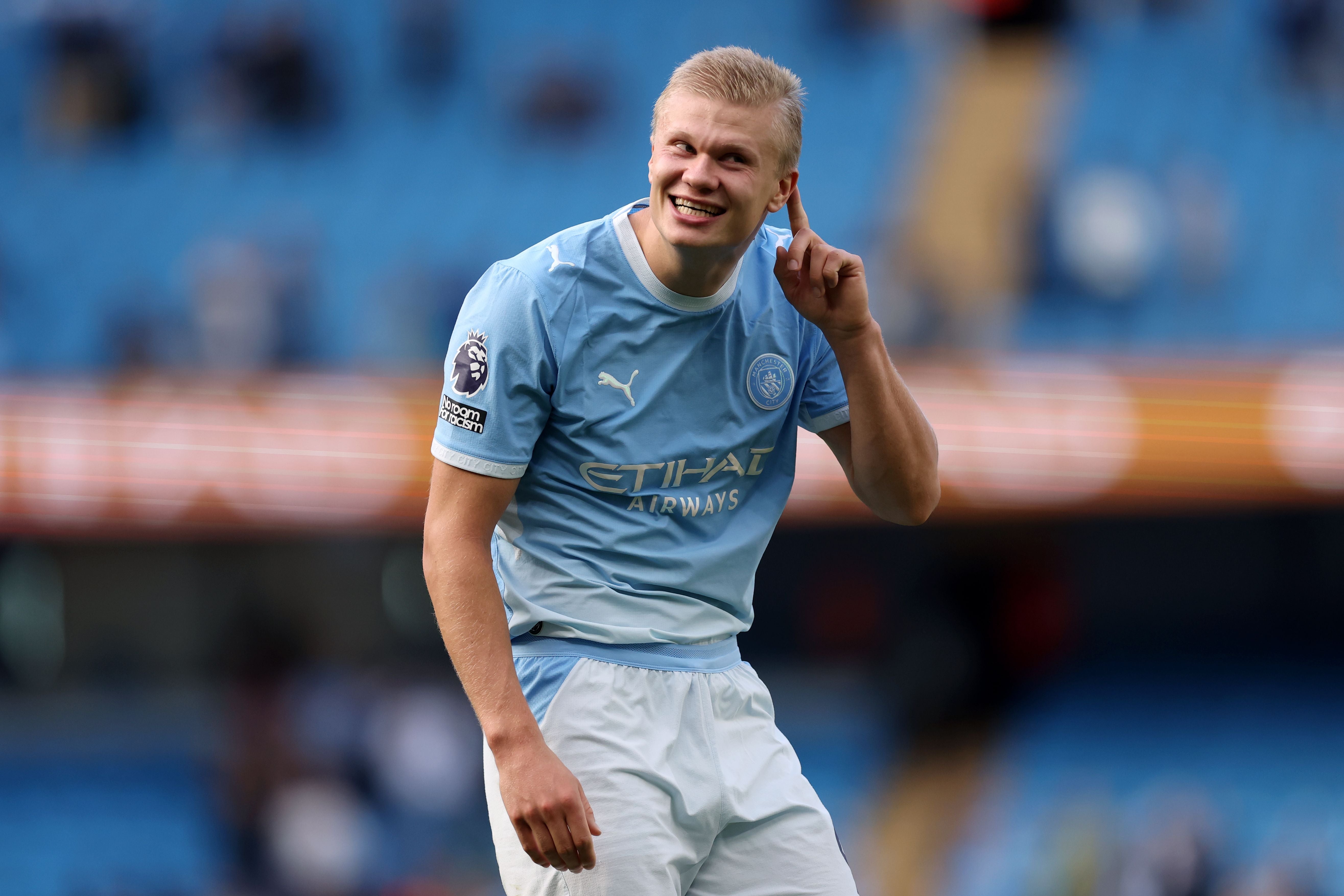 Ein Fußballspieler im Manchester City-Trikot lächelt und tippt sich ans Ohr auf dem Spielfeld.