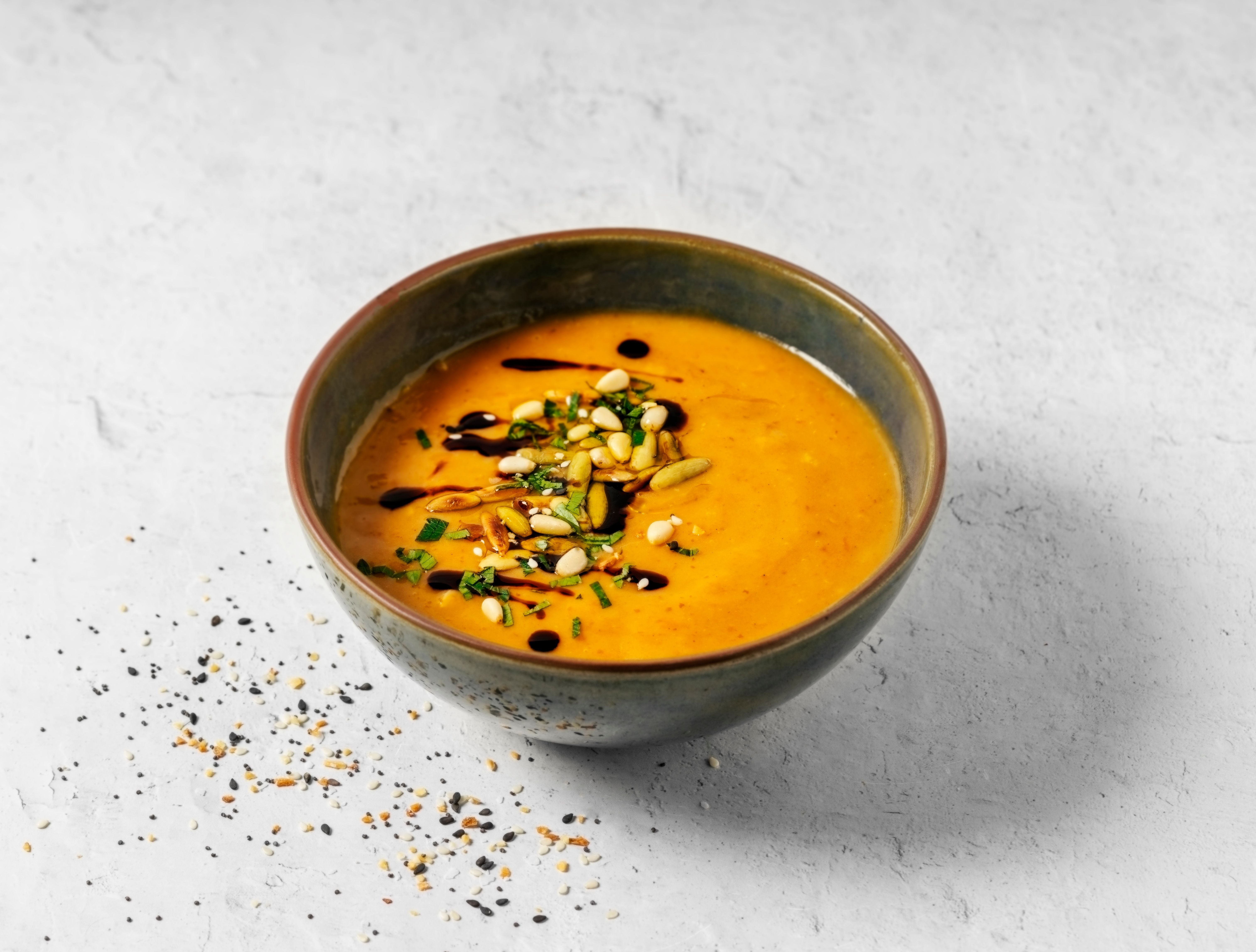 Schüssel mit cremiger Kürbissuppe, belegt mit Kernen, Kräutern und Balsamico-Tropfen.
