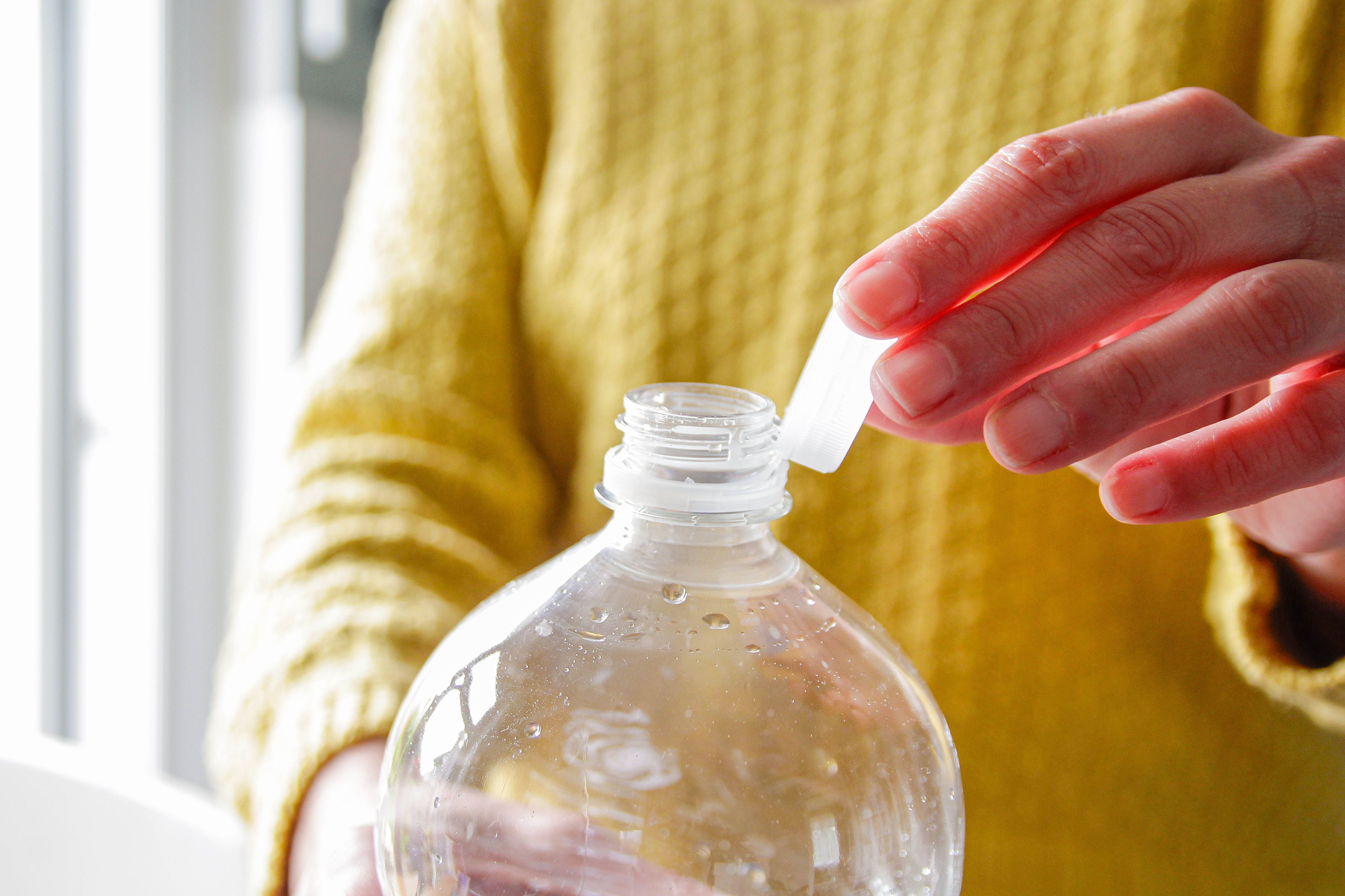 Eine Person hält eine Plastikflasche und berührt den daran befestigten Deckel.
