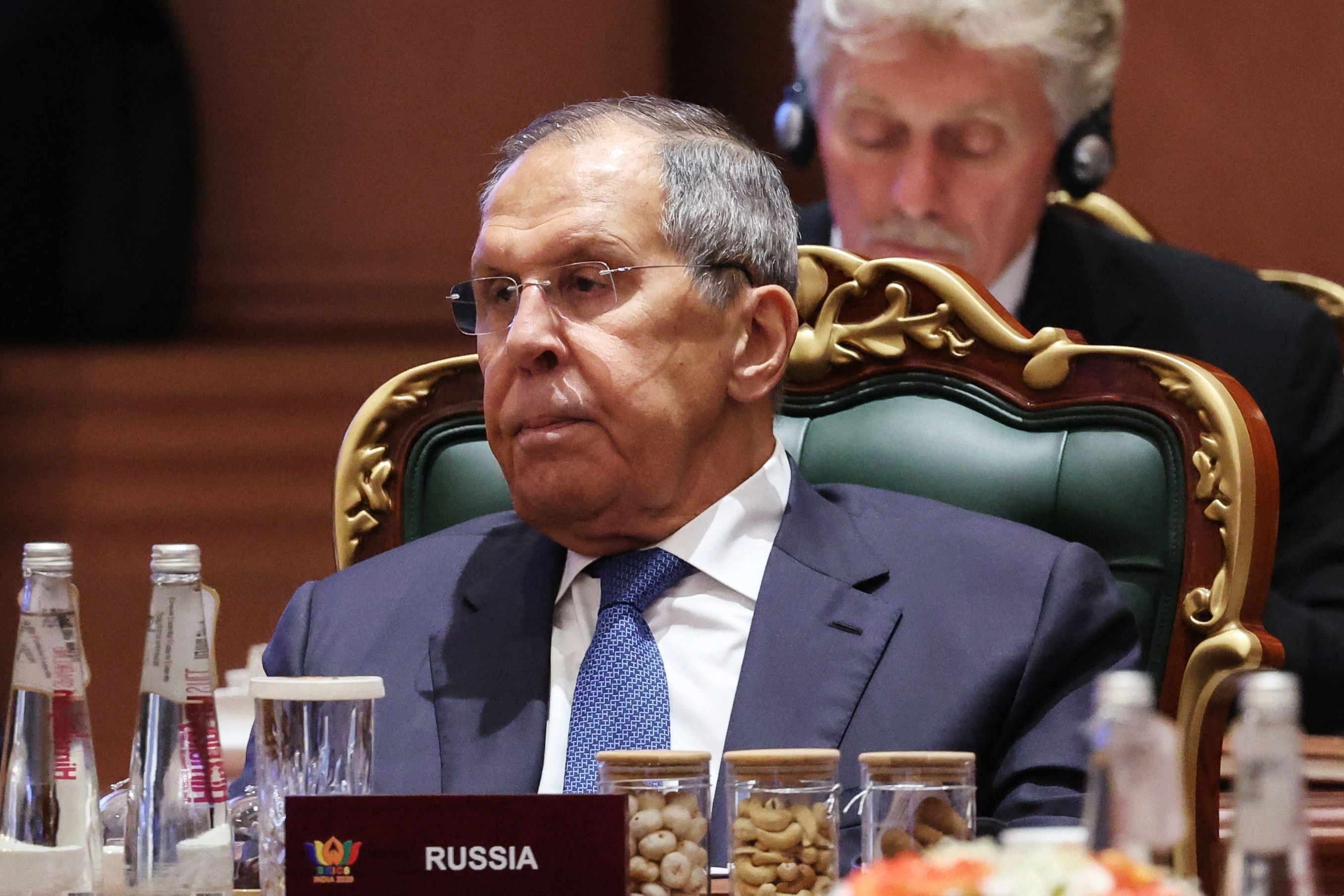 Ein älterer Mann im Anzug sitzt bei einer Konferenz am Tisch, vor ihm steht ein Schild mit „Russia“.