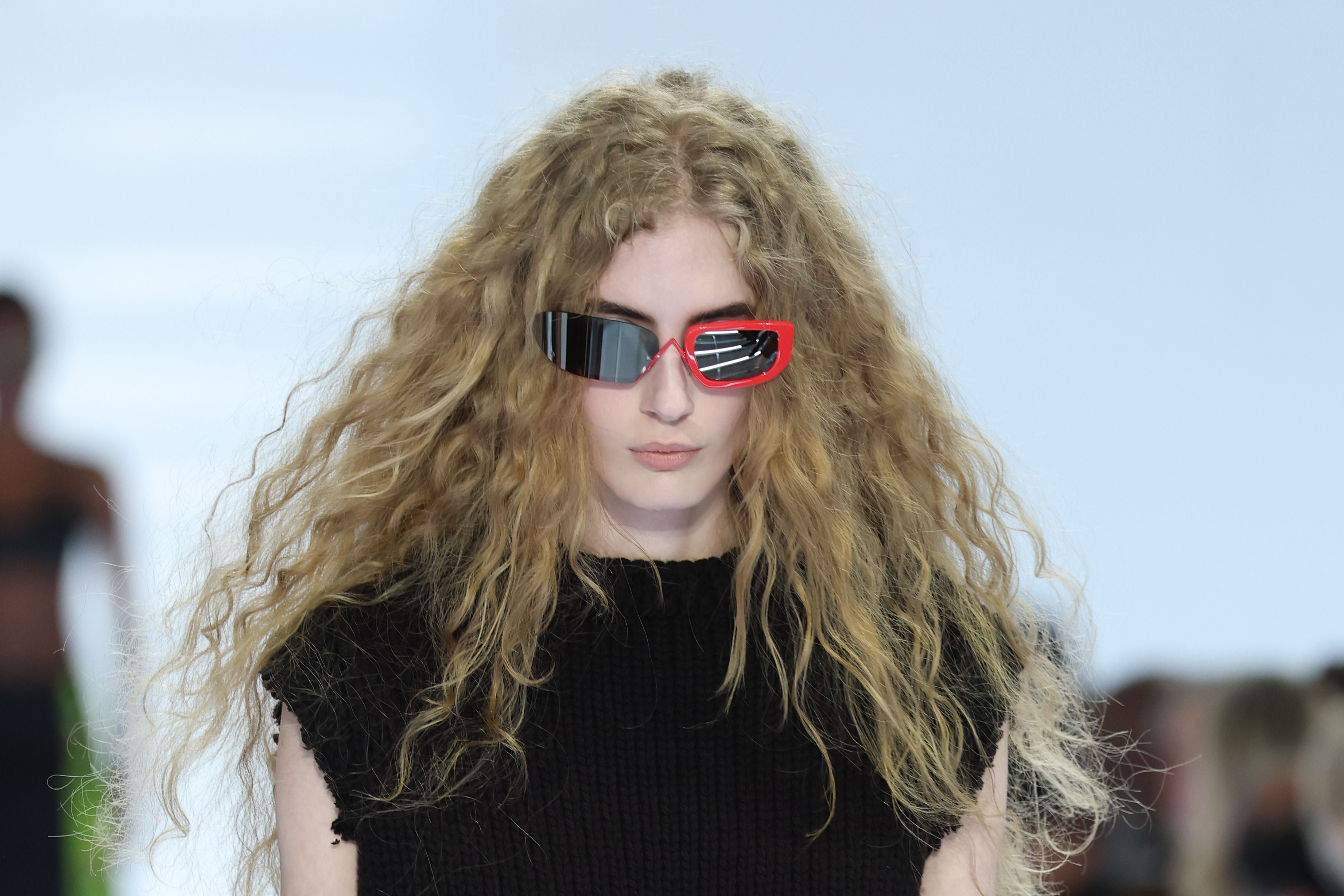 Model mit lockigem Haar und auffälliger, zweifarbiger Sonnenbrille auf dem Laufsteg.