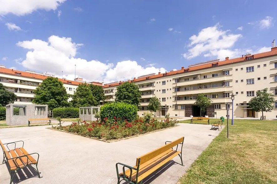 Innenhof des Karl-Marx-Hofs in Wien mit Bänken, Blumenbeeten und umgebenden Wohngebäuden.