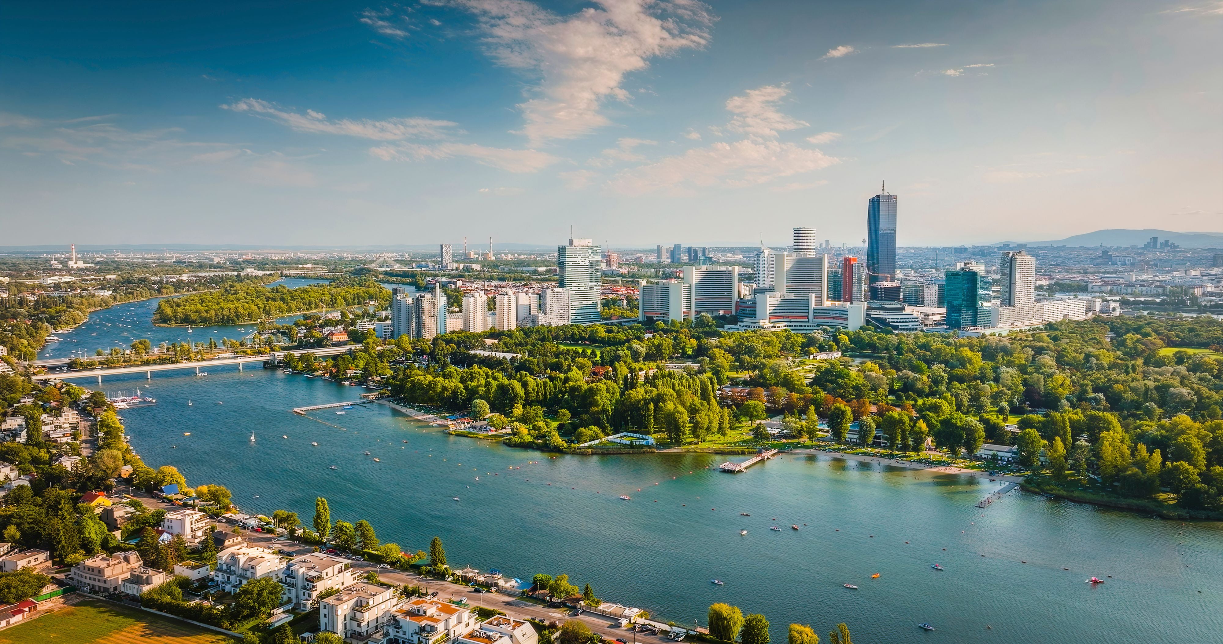 Luftaufnahme von Wien mit moderner Skyline, Donauinsel und Donau an einem sonnigen Tag.