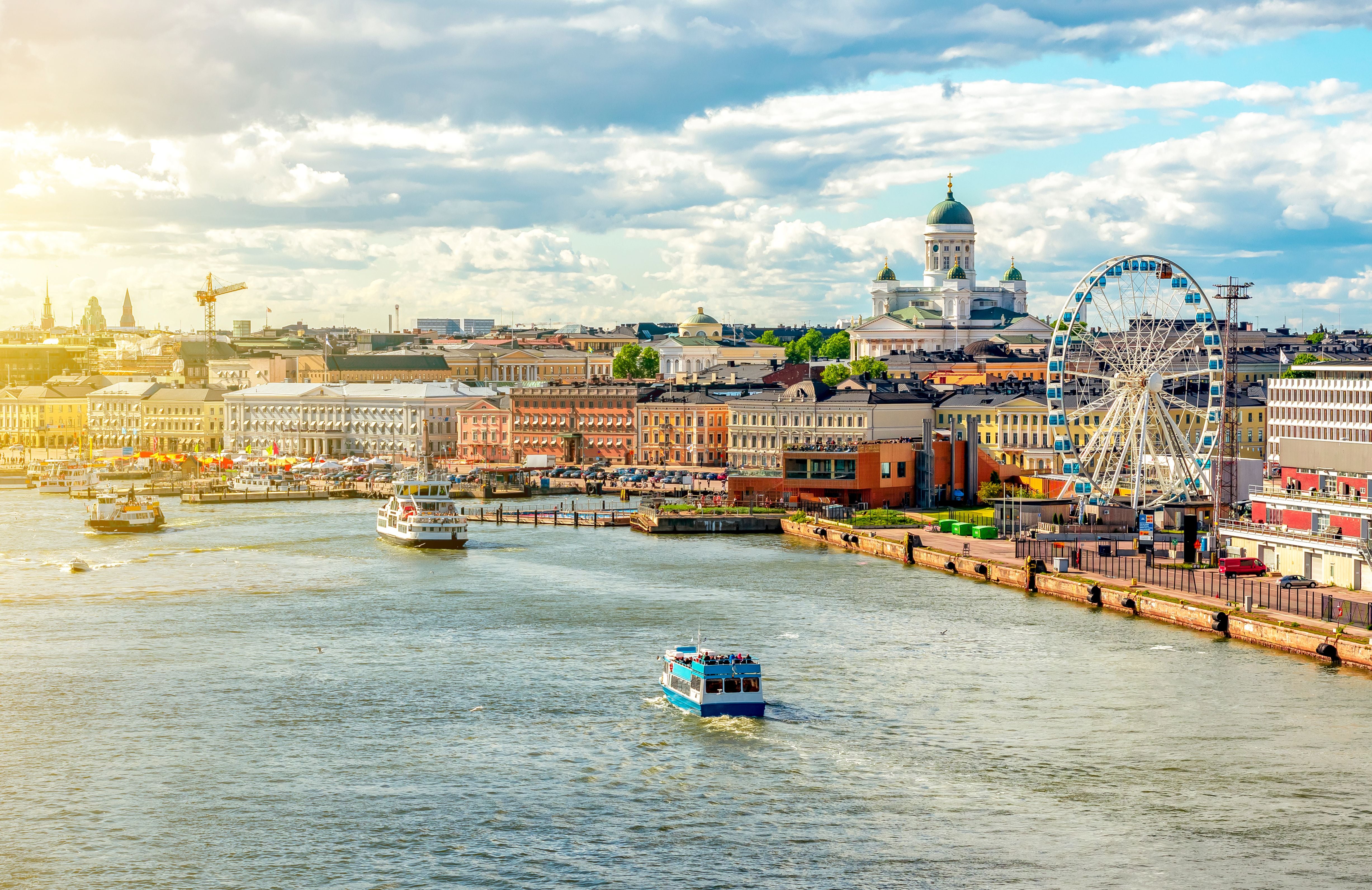 Stadtansicht von Helsinki mit Dom, Riesenrad und Marktplatz am Wasser bei Sonnenschein.