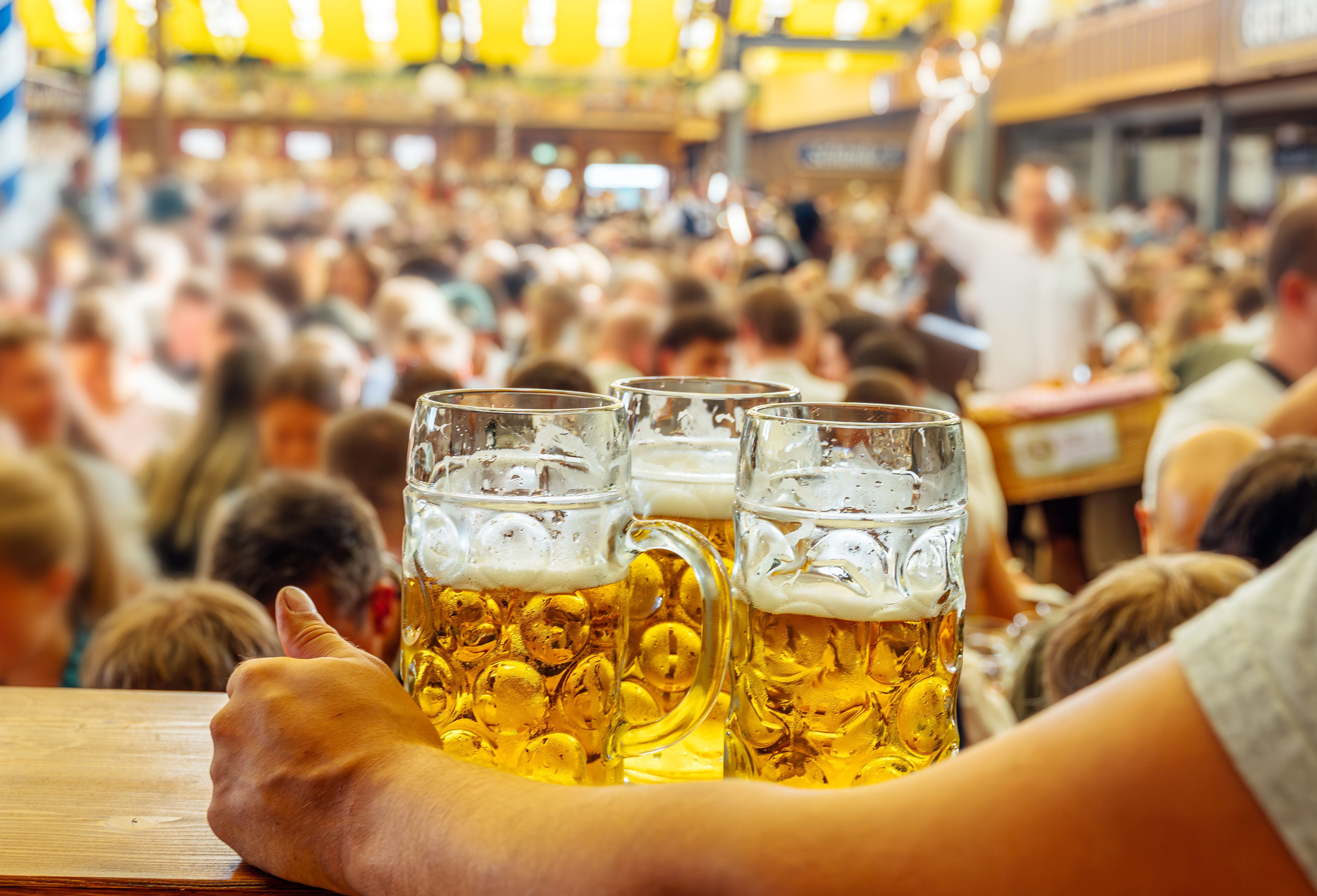 Drei Maß Bier werden auf einem Oktoberfest mit vielen feiernden Menschen serviert.