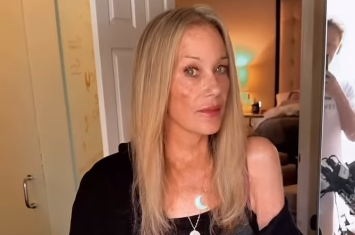 Eine Frau mit langen blonden Haaren steht in einem Zimmer vor einem Spiegel.
