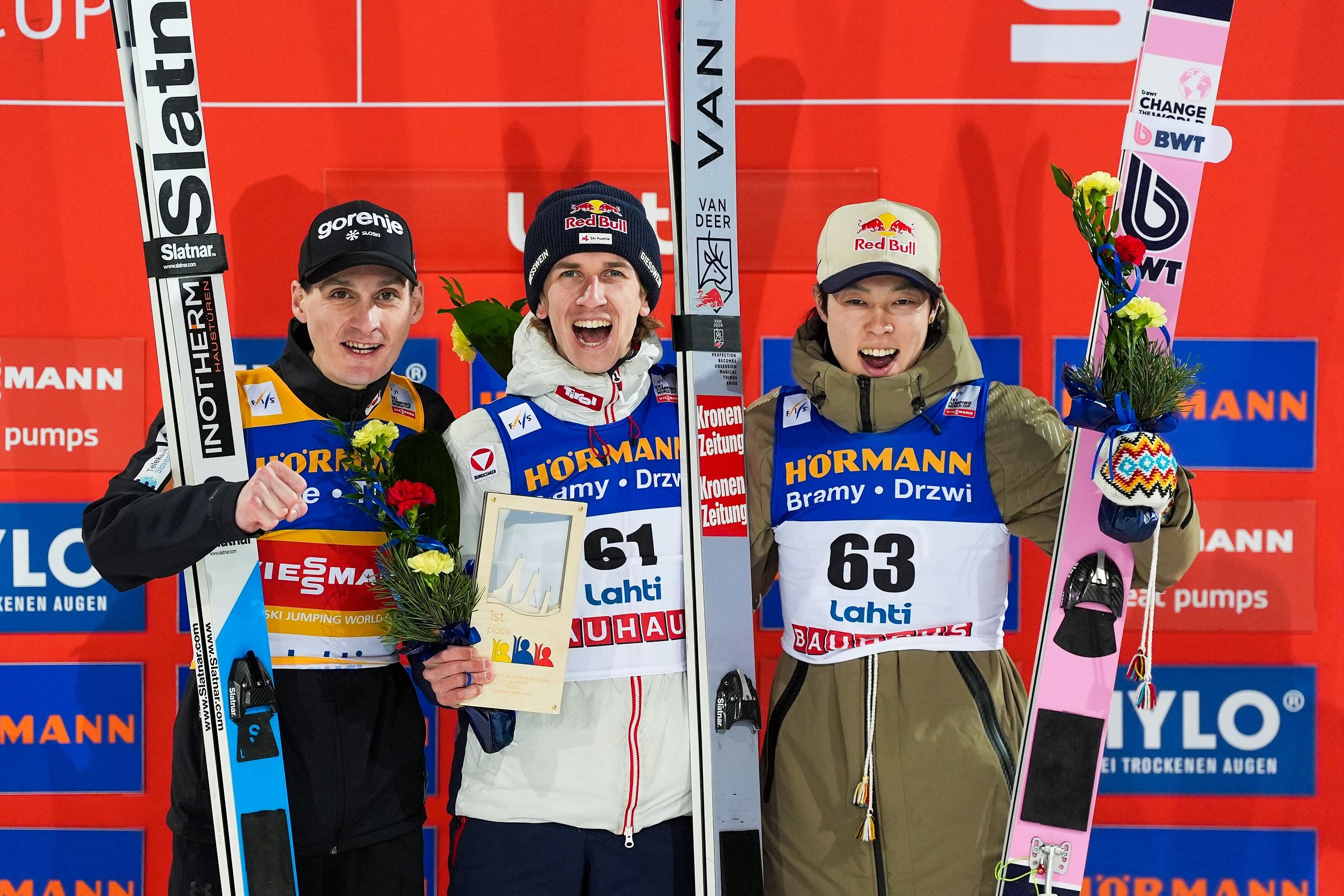Domen Prevc, Daniel Tschofenig und Ryoyu Kobayashi stehen jubelnd mit ihren Skiern auf dem Siegerpodest.