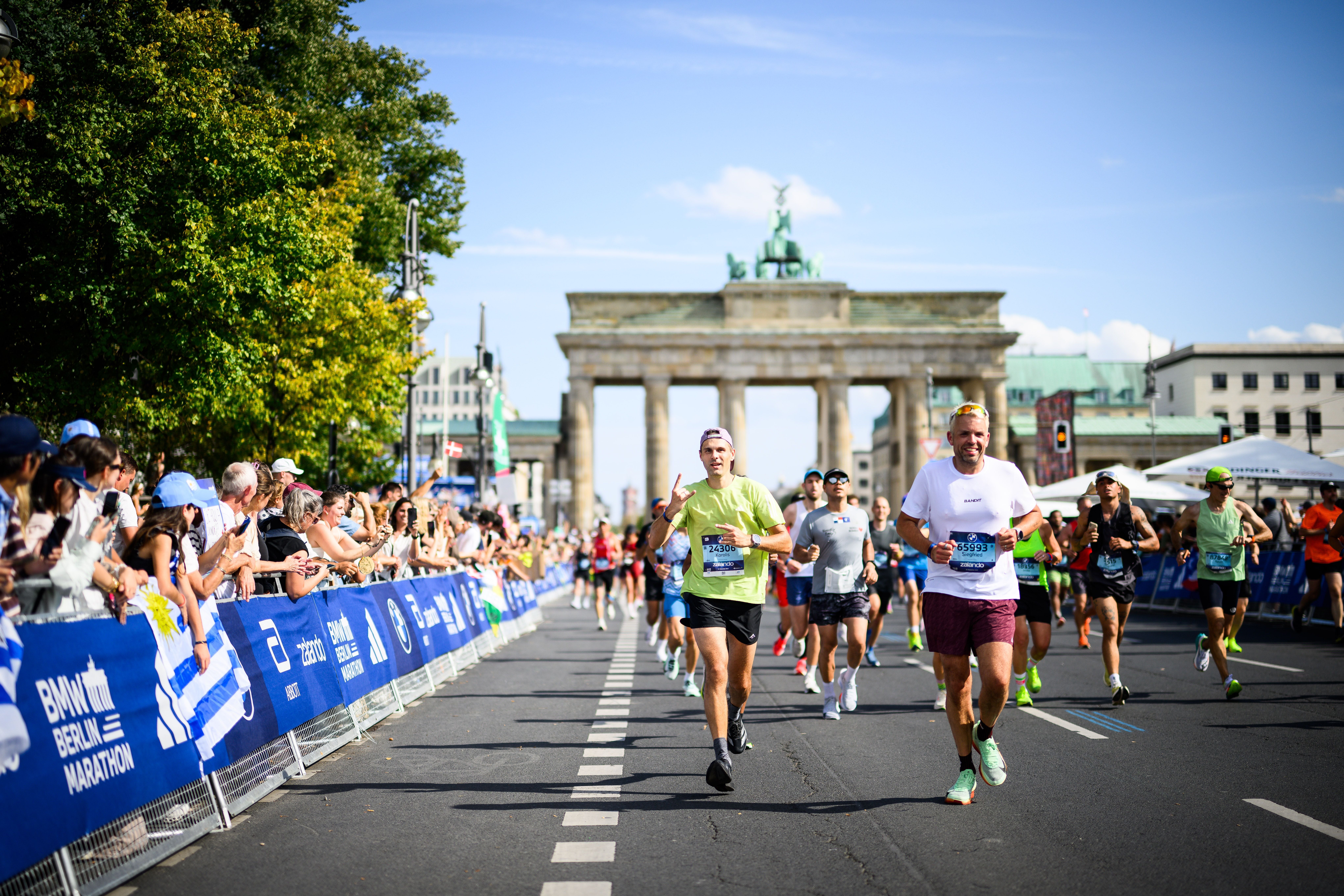 Läufer passieren das Brandenburger Tor beim BMW Berlin-Marathon, Zuschauer jubeln am Rand.
