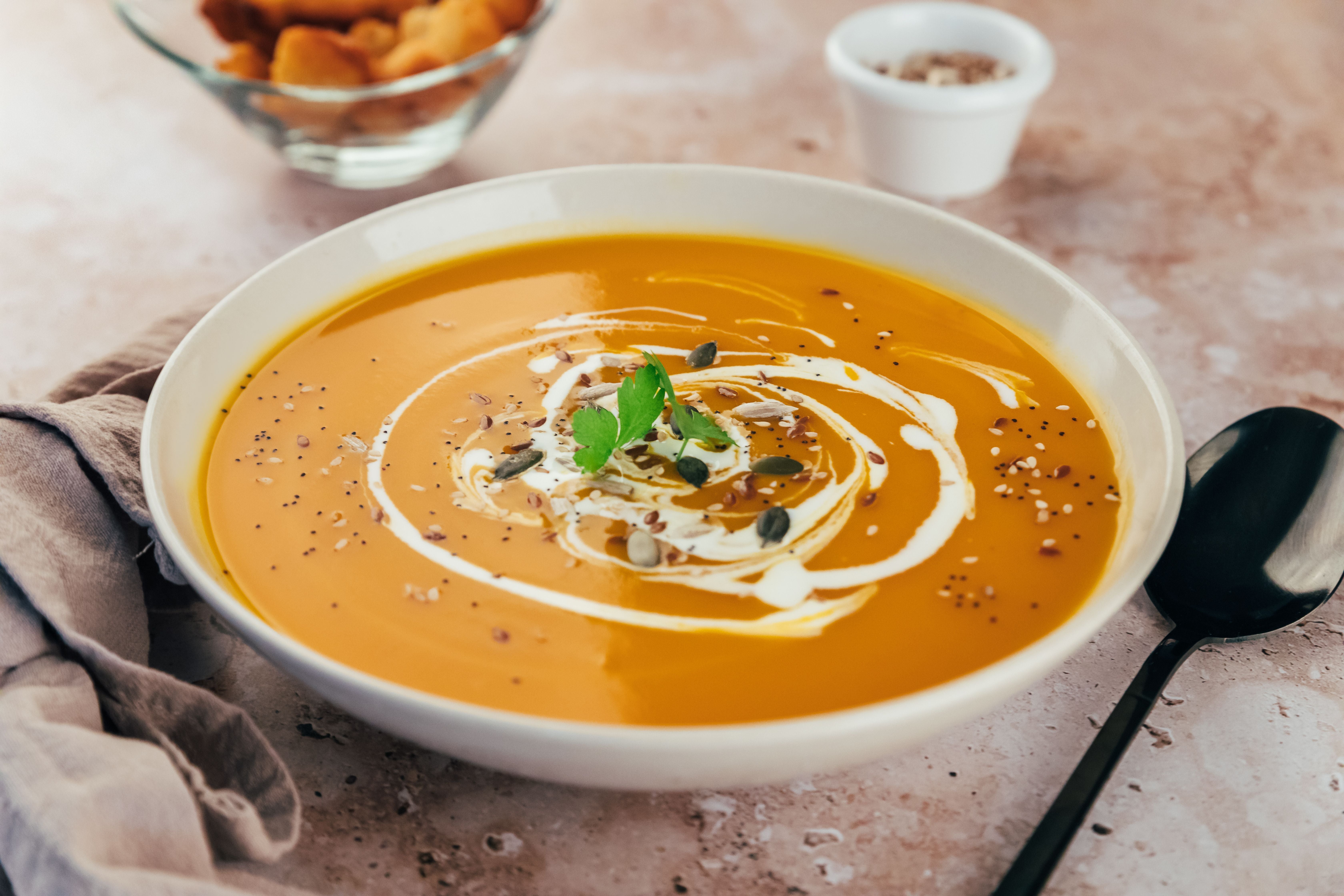 Kürbissuppe mit Sahne, Kernen und Petersilie in einer weißen Schale auf braunem Untergrund.