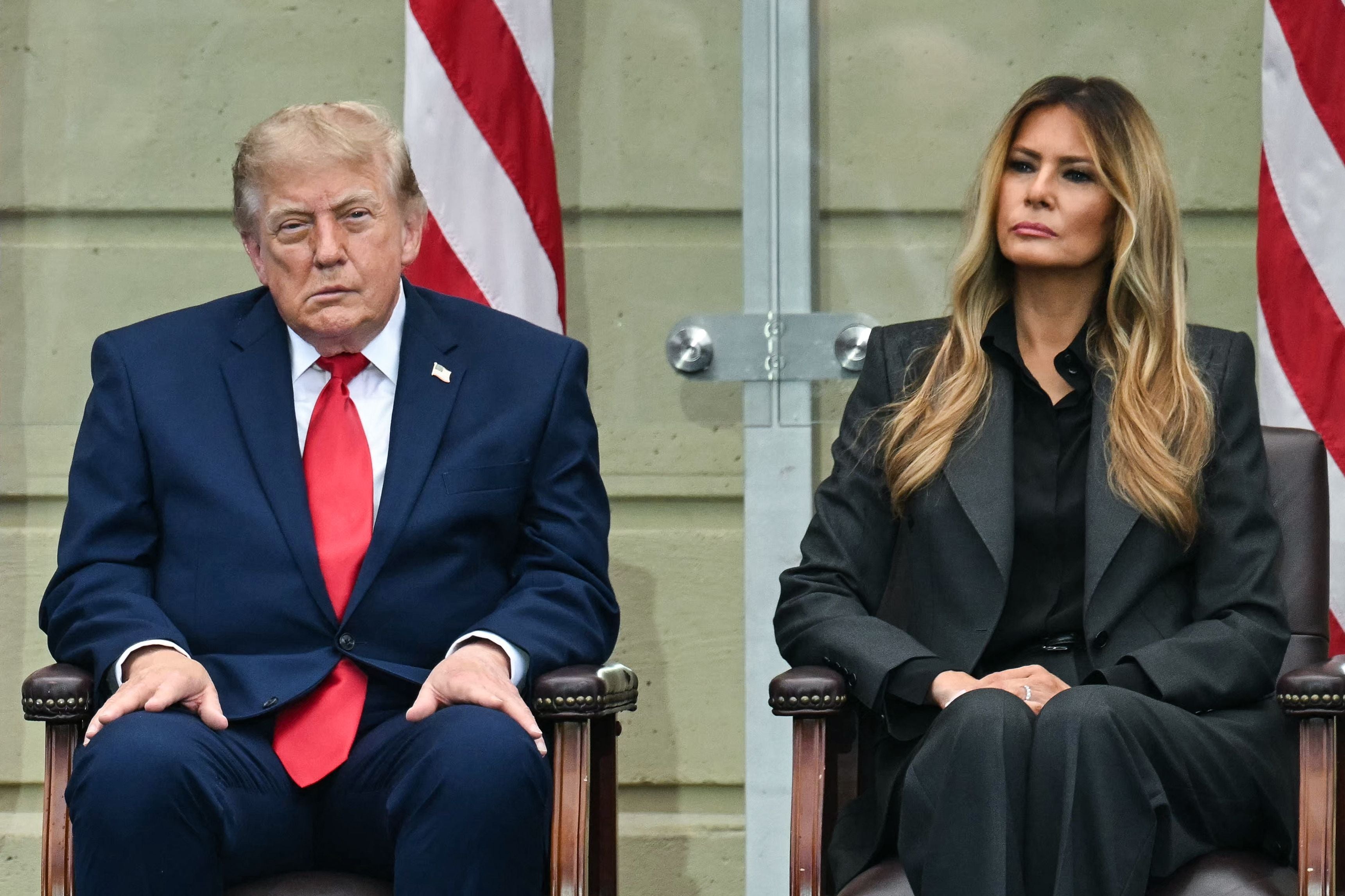 Ein Mann im Anzug und eine Frau im Hosenanzug sitzen nebeneinander vor US-Flaggen.