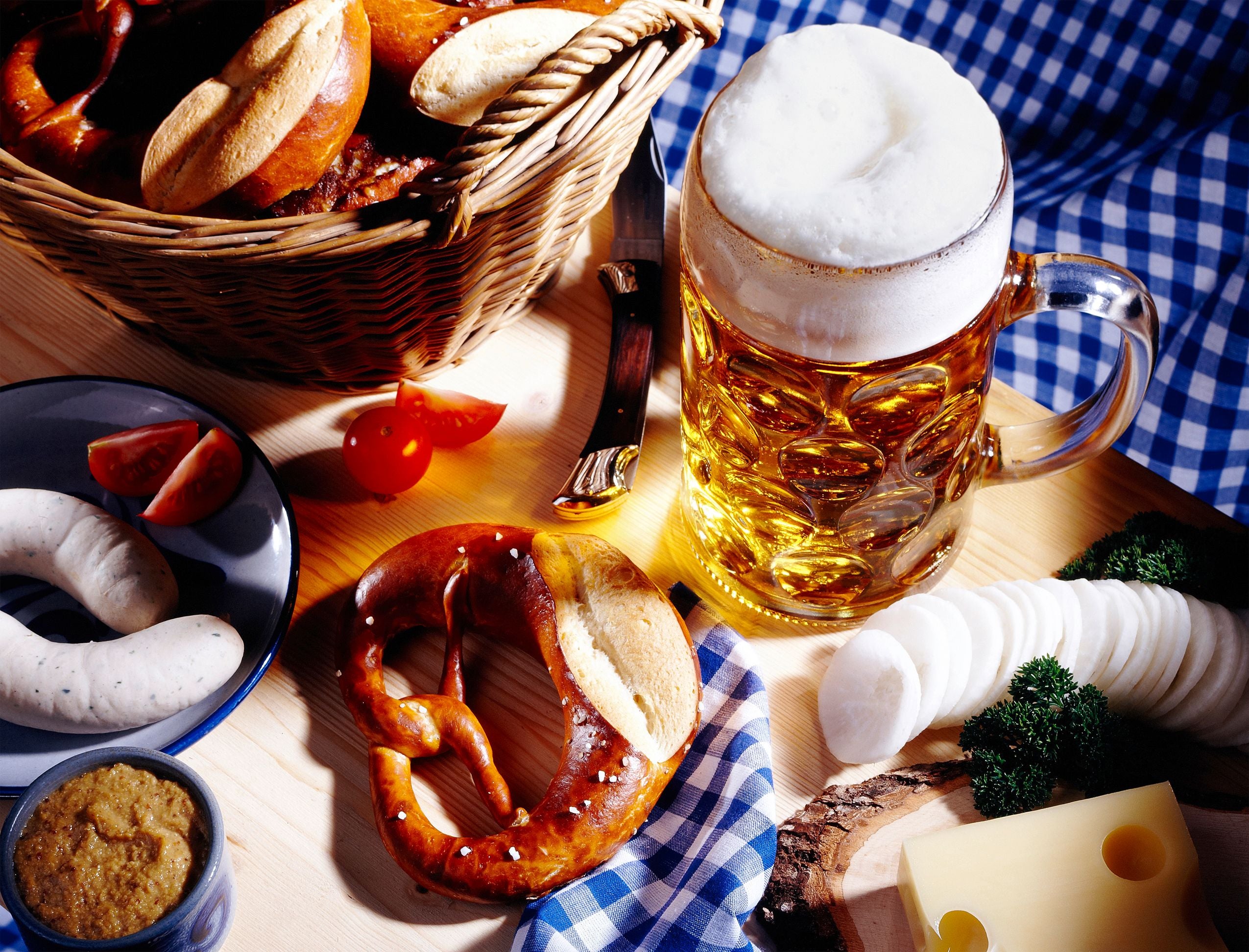Bayerisches Brotzeit mit Breze, Weißwurst, Radi, Käse, Senf und Maß Bier auf Holztisch.