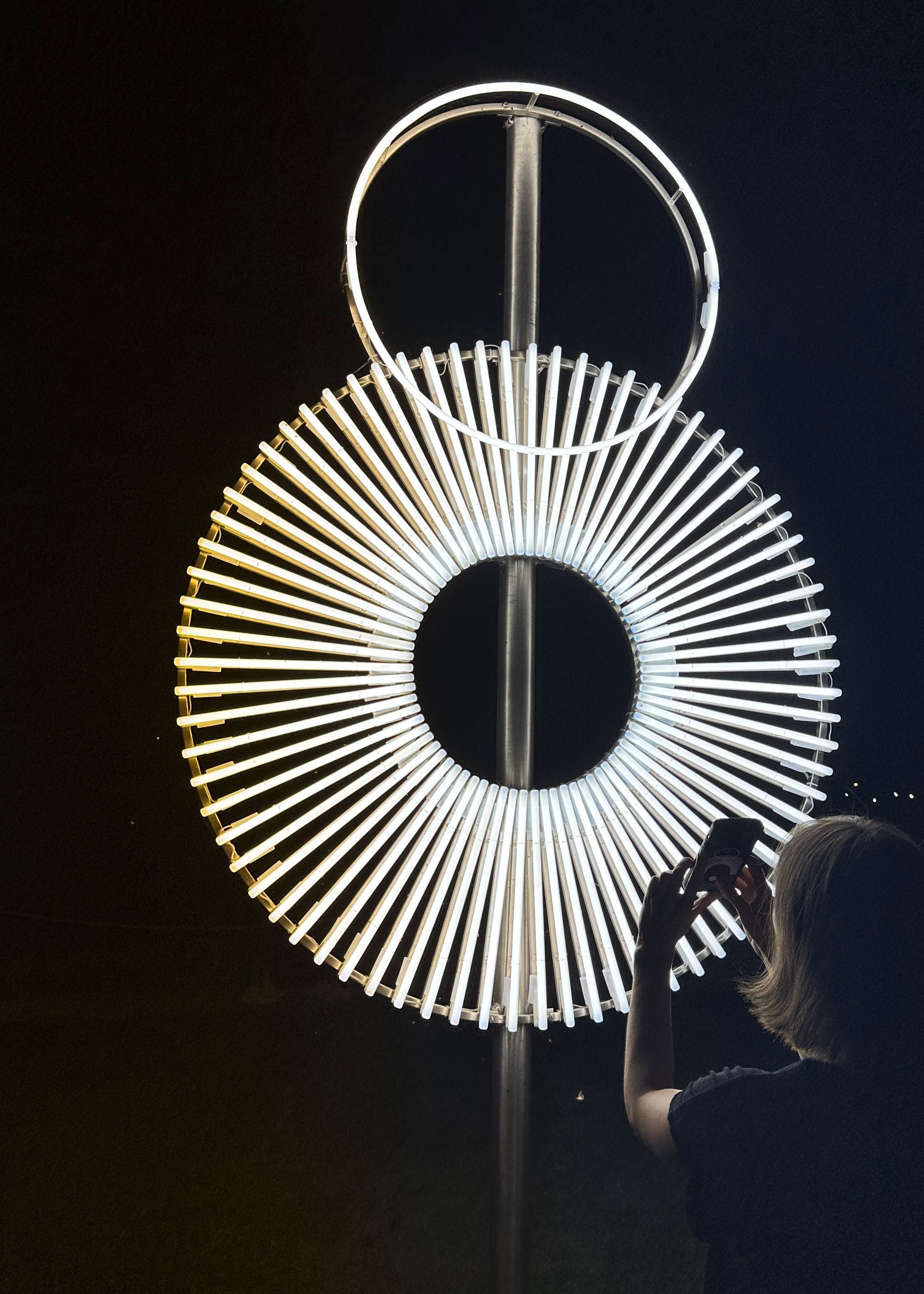 Frau fotografiert nachts die leuchtende Lichtskulptur "Terre Roulànte" von Miriam Hamann.