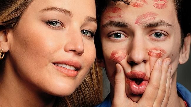 Frau lächelt in die Kamera, neben ihr ein Mann mit Lippenstiftabdrücken im Gesicht.
