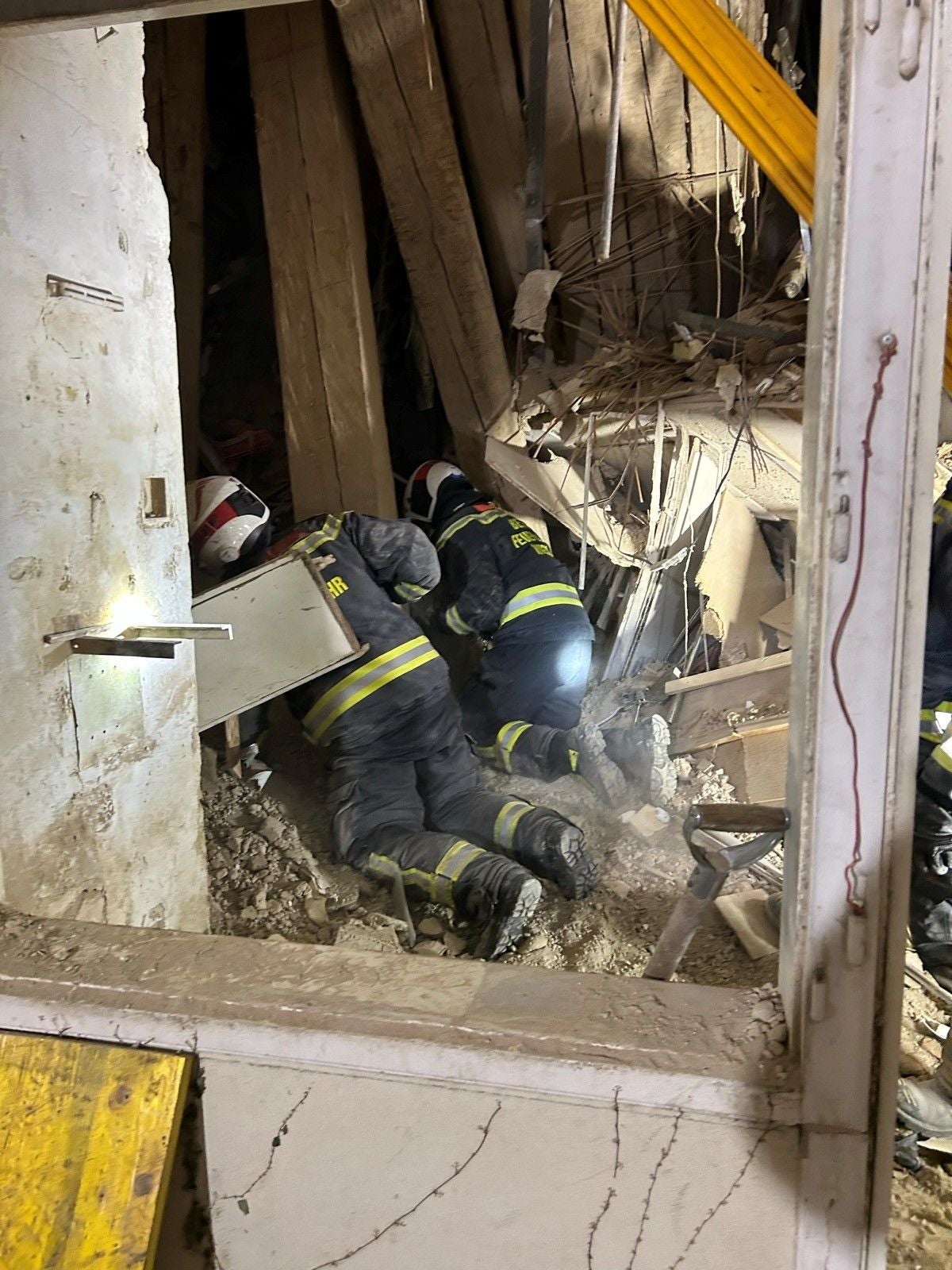 Mehrere Einsatzkräfte arbeiten inmitten eingestürzter Holzbalken und Trümmern in einem Gebäude.