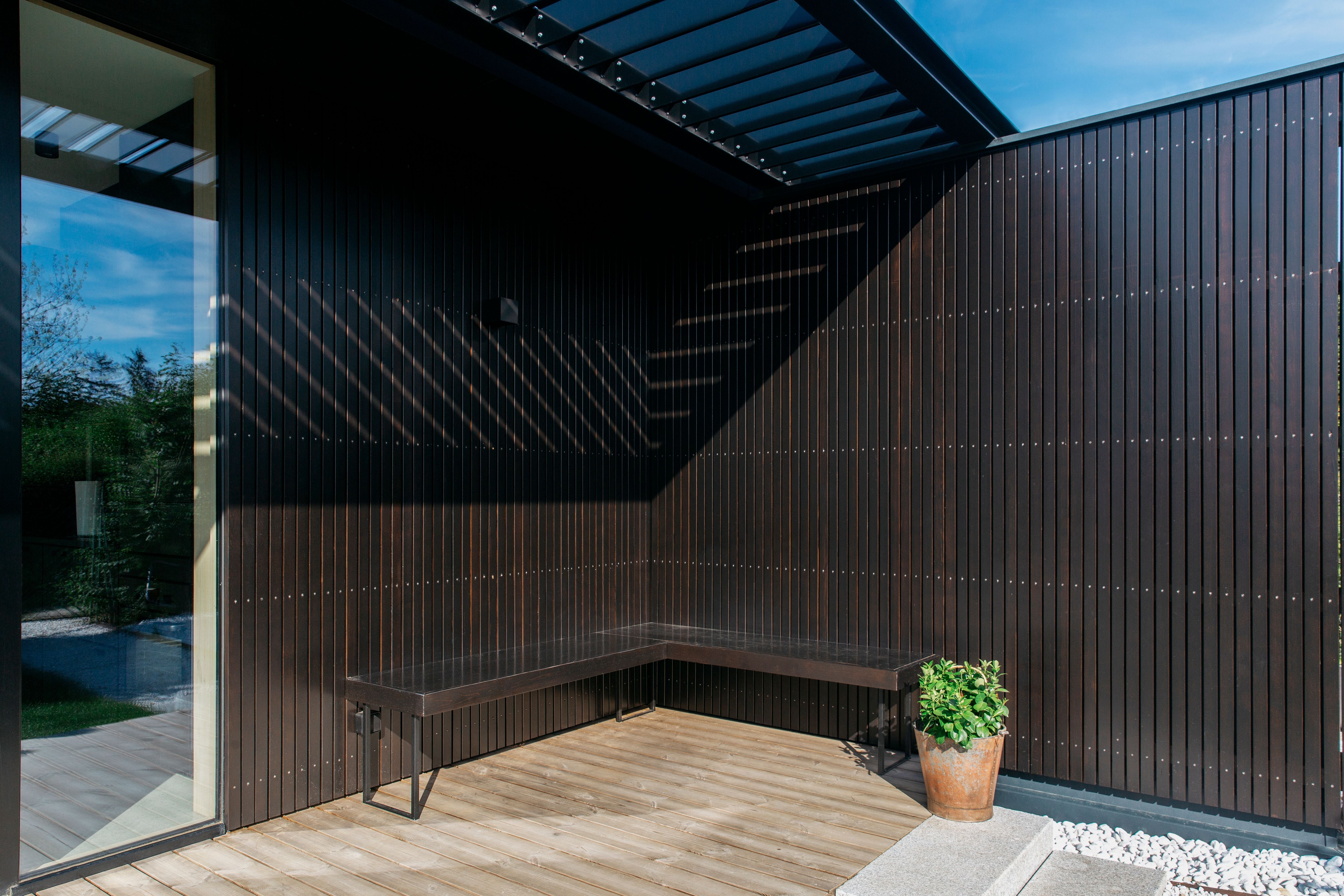 Moderne Terrasse mit dunkler Holzverkleidung, L-förmiger Bank und Topfpflanze in der Ecke.