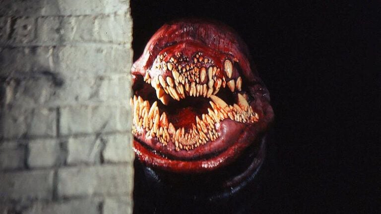 Ein großes, monsterhaftes Maul mit vielen scharfen Zähnen schaut um eine Mauerkante.