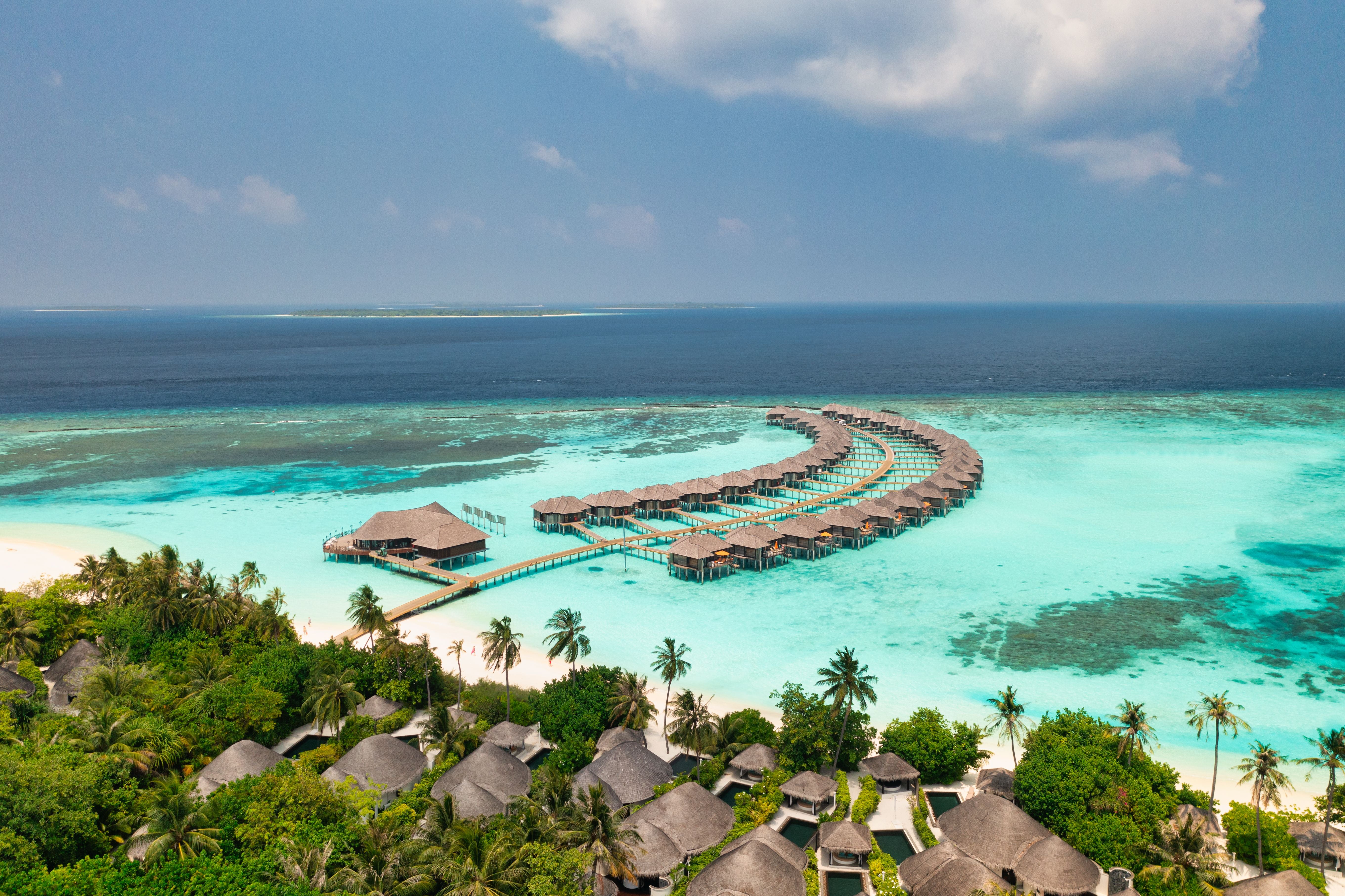 Luftaufnahme von Wasser-Villen auf Stelzen im türkisblauen Meer der Malediven mit Palmenstrand.
