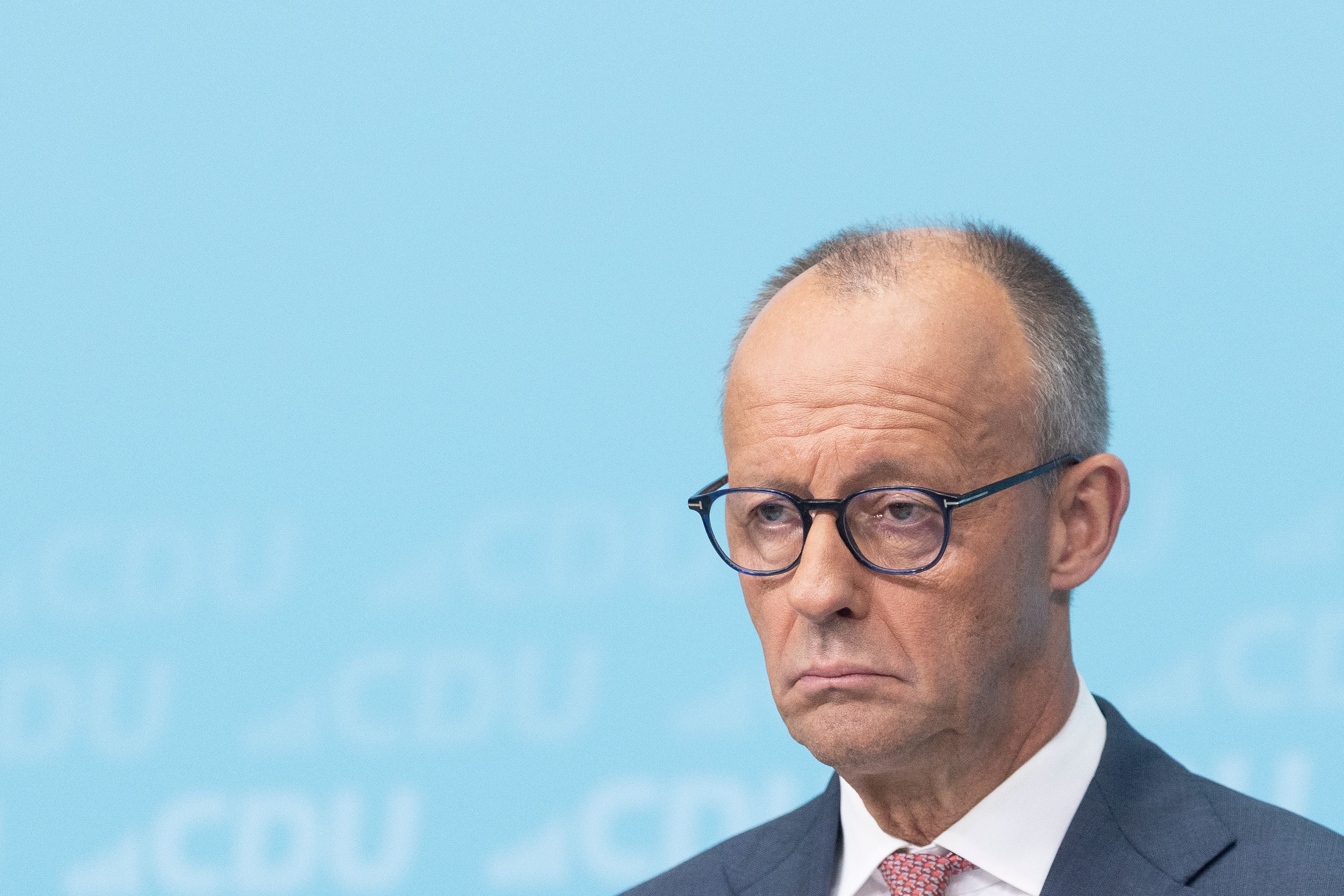 Ein Mann im Anzug mit ernster Miene spricht vor hellblauem CDU-Hintergrund.