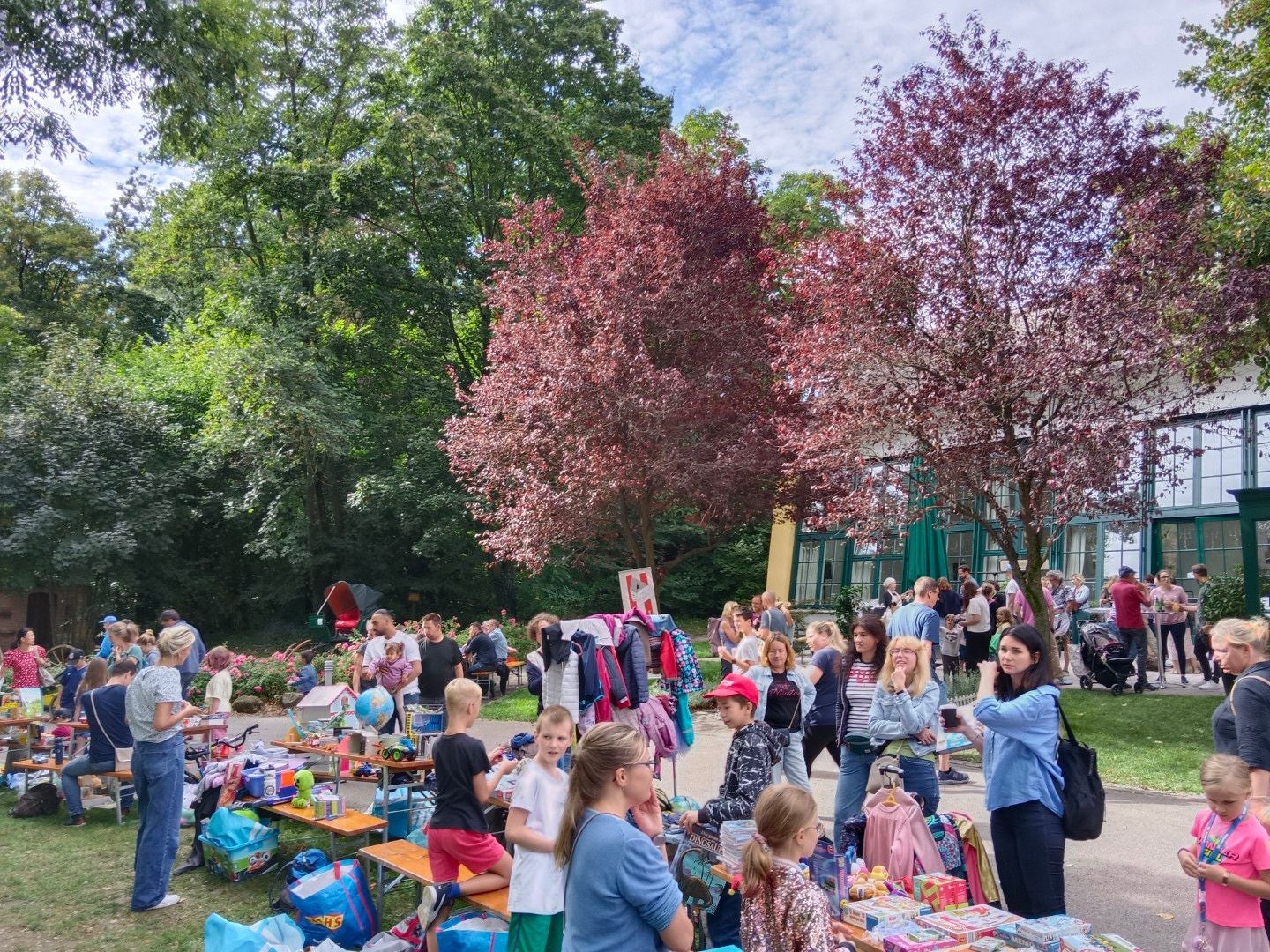 Menschen verkaufen und kaufen Spielsachen auf einem Flohmarkt im Park bei herbstlichen Bäumen.