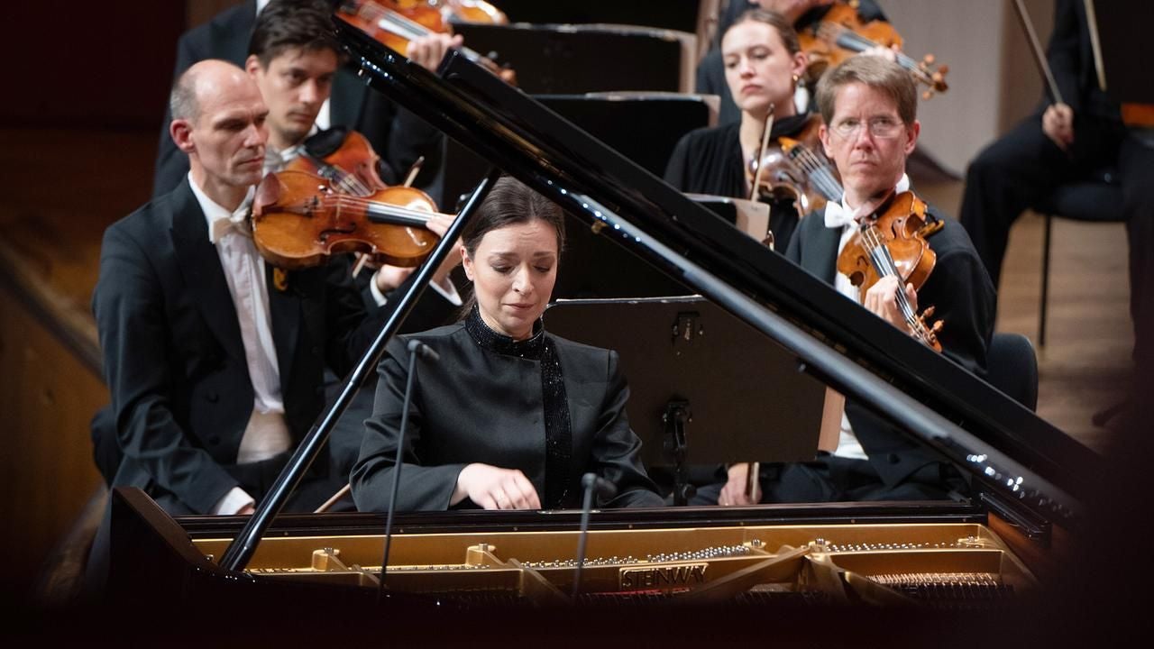 Eine Pianistin spielt am Flügel, begleitet von einem Orchester mit Streichinstrumenten.