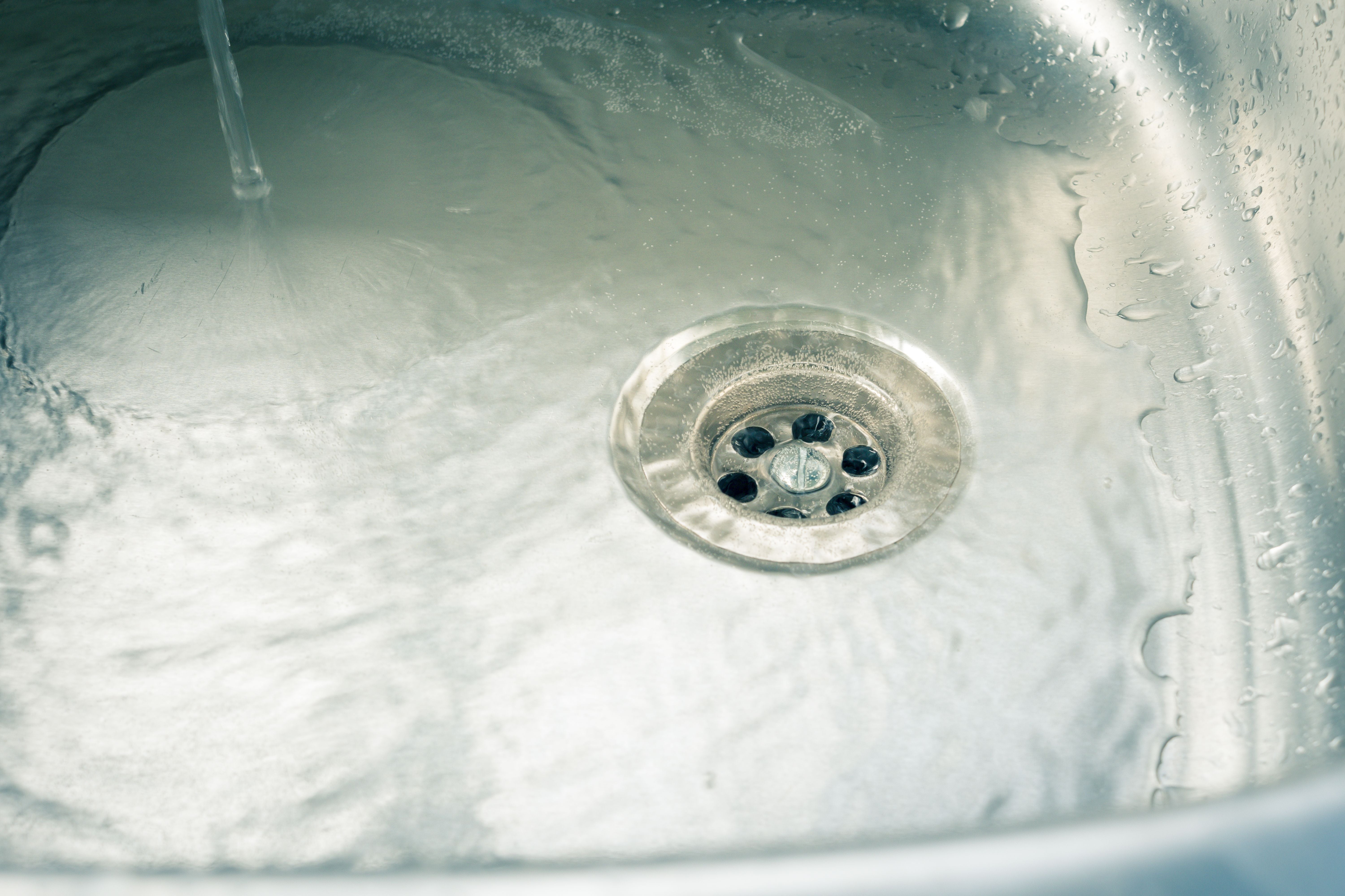 Wasser läuft in ein sauberes Metallspülbecken mit sichtbarem Abfluss.