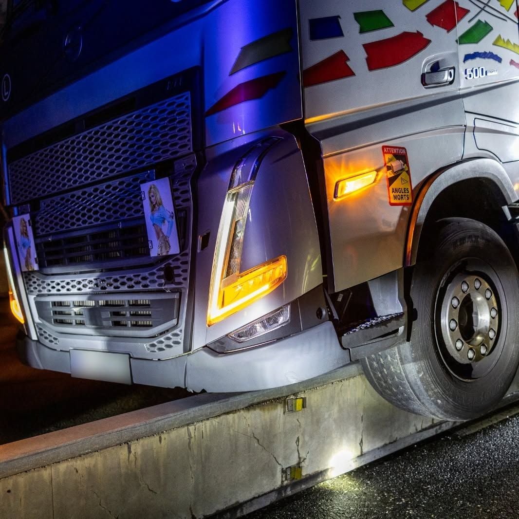 Ein Lkw ist bei Nacht auf eine Betonleitplanke geraten, das Vorderrad hängt über dem Rand.