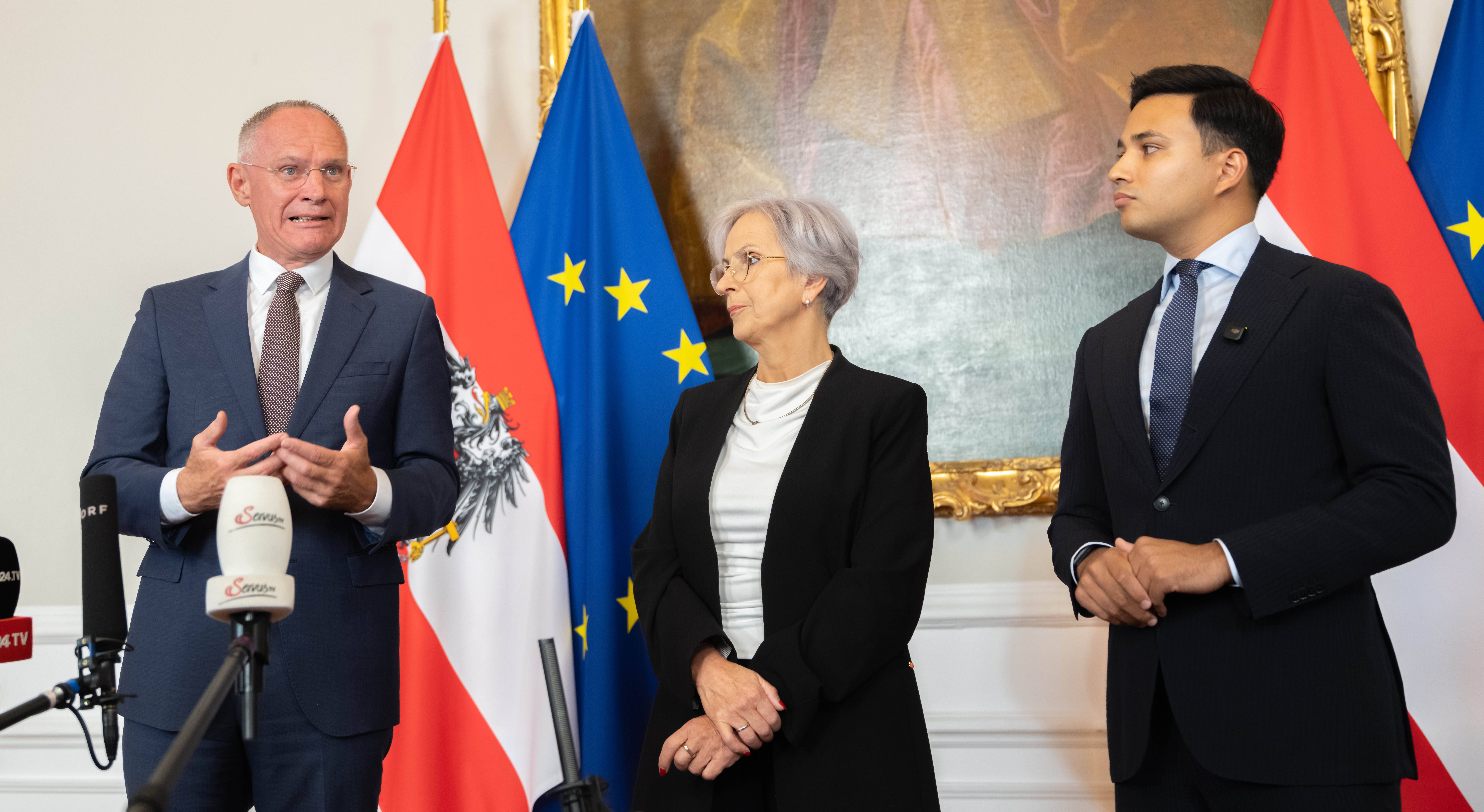 Drei Politiker sprechen bei einer Pressekonferenz vor österreichischer und EU-Flagge in Wien.