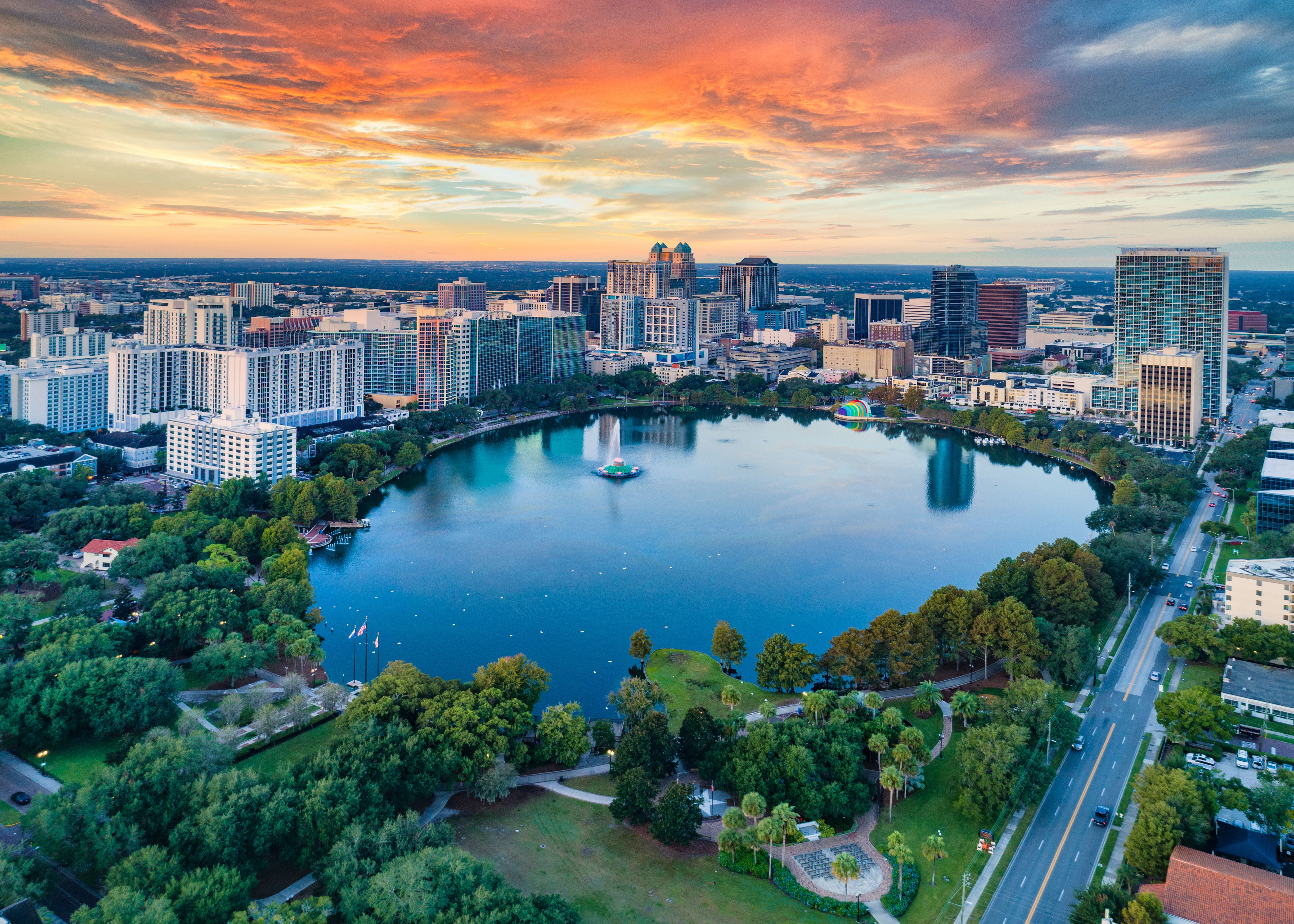 Drohnenaufnahme von Orlando mit See, Hochhäusern und farbenfrohem Sonnenuntergang.