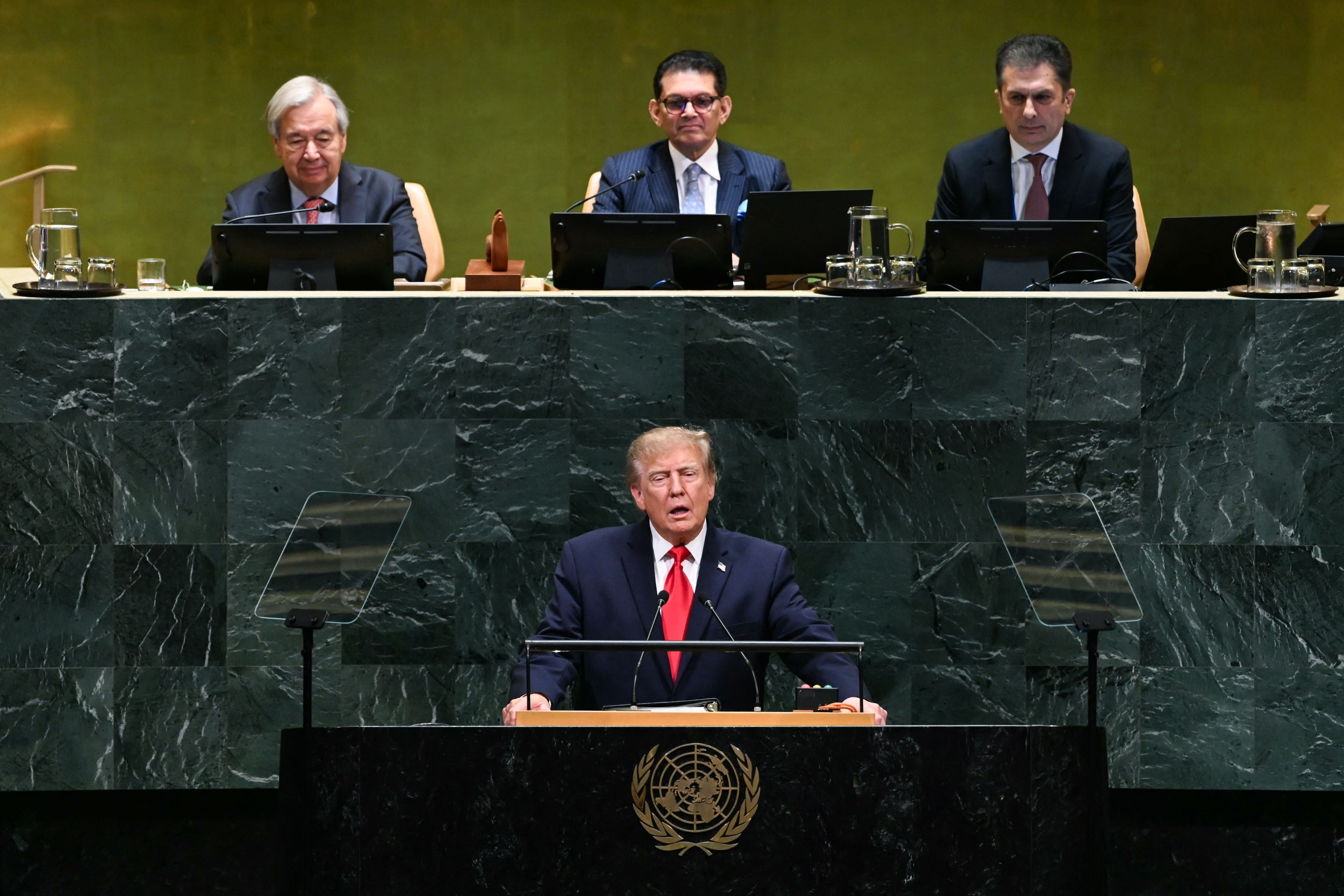 Ein Mann hält eine Rede am Rednerpult der Vereinten Nationen, drei Personen sitzen dahinter.