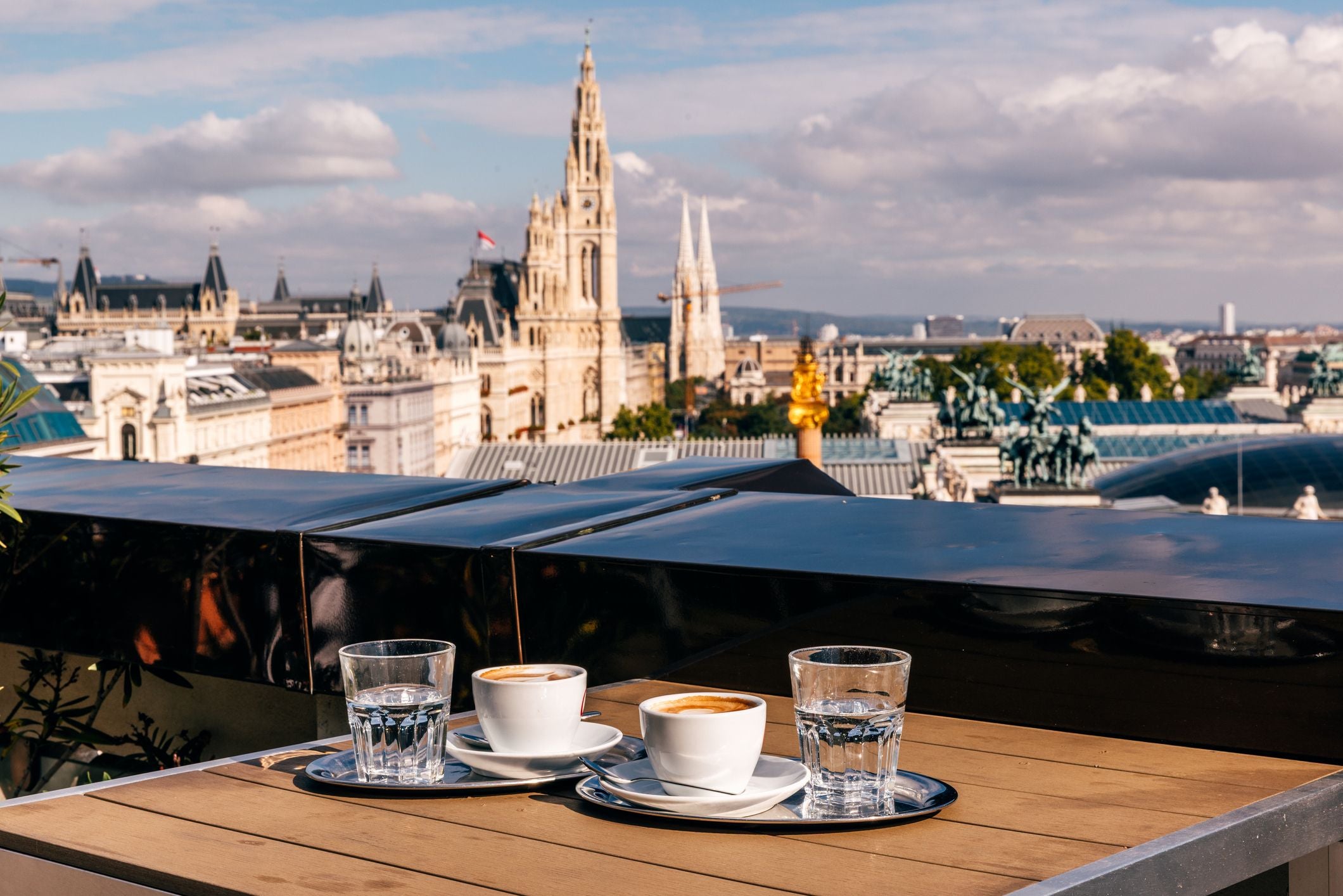 Zwei Tassen Kaffee und zwei Gläser Wasser auf einem Tisch mit Blick auf Wiens Altstadt und Rathaus.