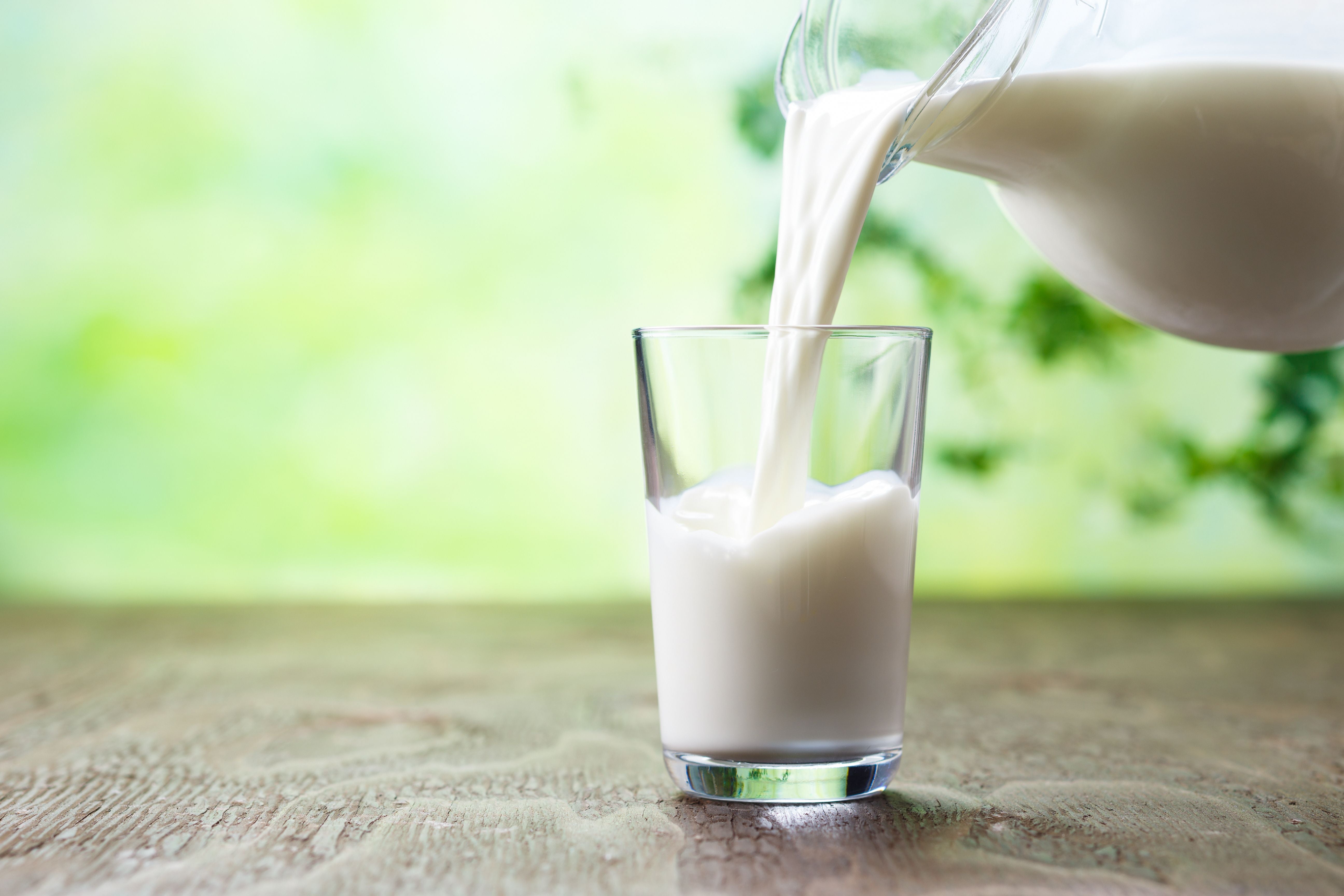 Milch wird aus einem Krug in ein Glas auf einem Holztisch gegossen.