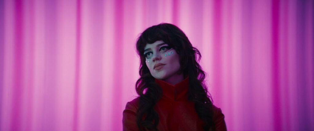 Frau mit Glitzerschminke vor pink-lila beleuchtetem Hintergrund beim Slash Filmfestival.