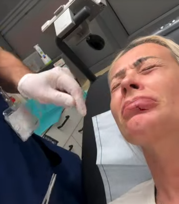 Frau mit schmerzverzerrtem Gesicht liegt auf einer Untersuchungsliege beim Arzt.