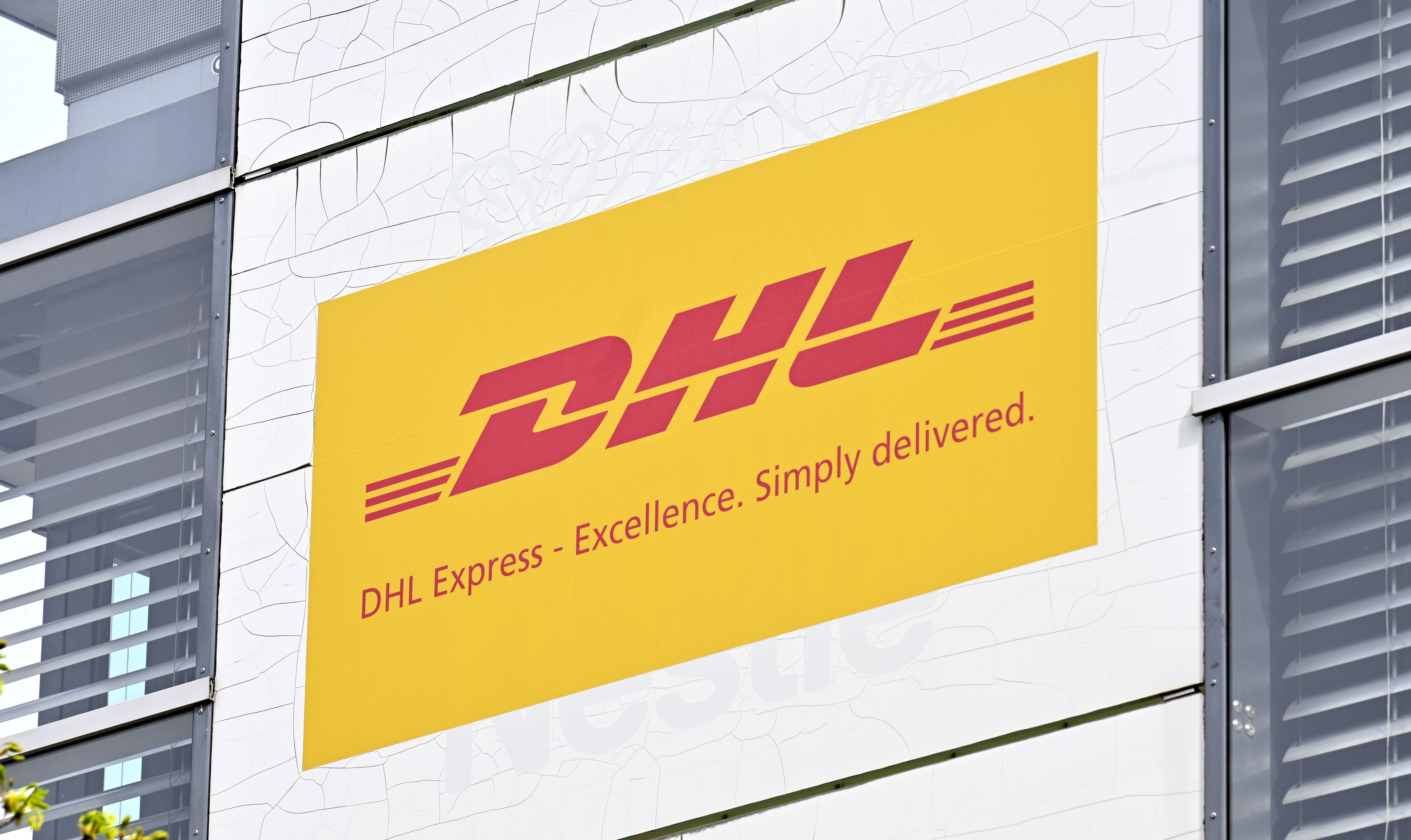 Gelbes DHL Express-Logo mit Slogan an einer Gebäudefassade in Wien.